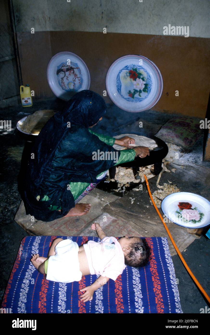 A villagel woman making bread on a small gas stove while her baby lies on a mat beside her OMAN Stock Photo