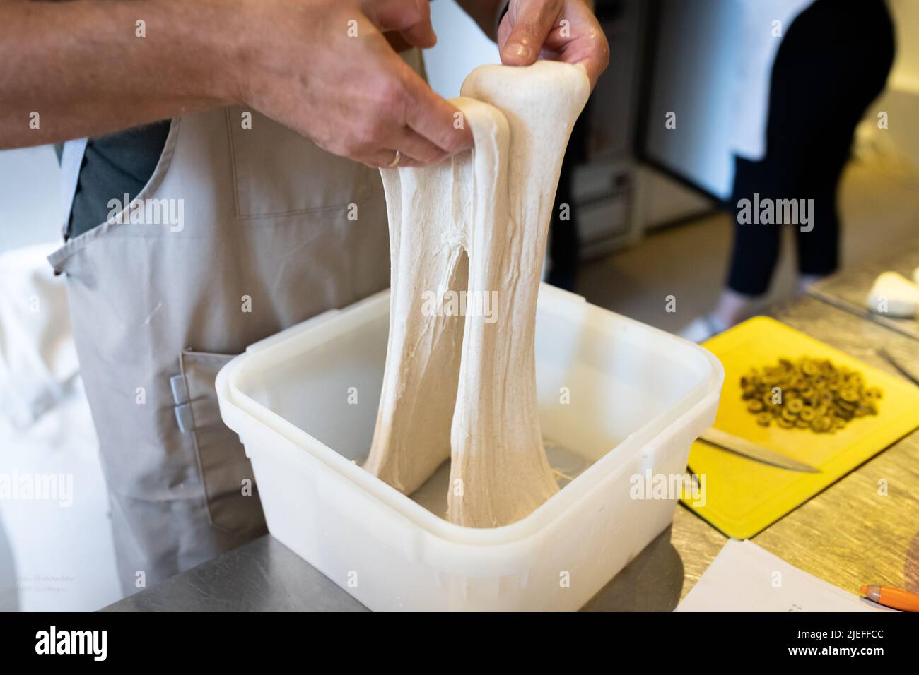 The process of making wheat bread in an artisan bakery. The folding of the dough during fermentation. Front view. Stock Photo