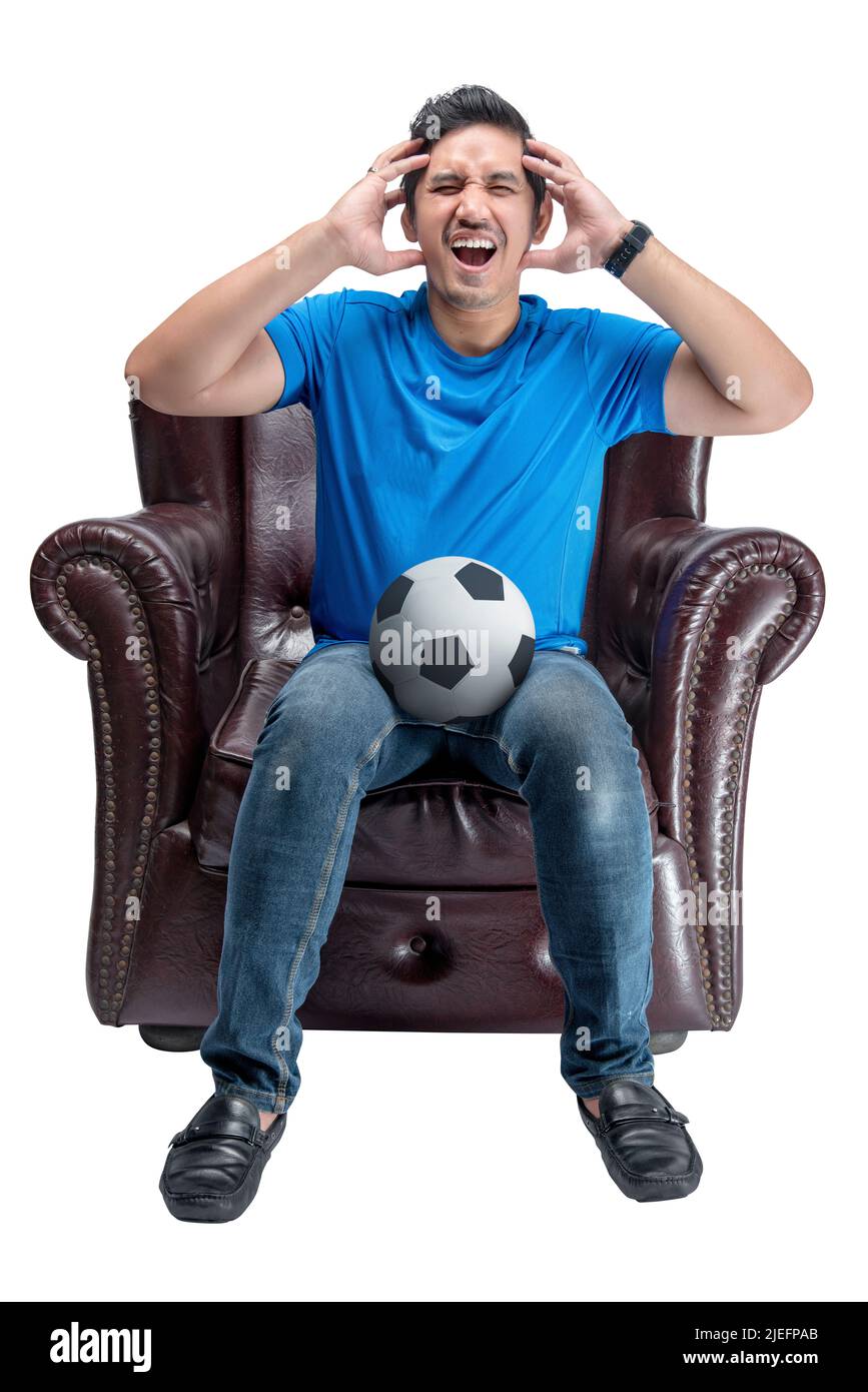 Asian man with the ball sitting on the couch with a disappointed expression isolated over white background Stock Photo