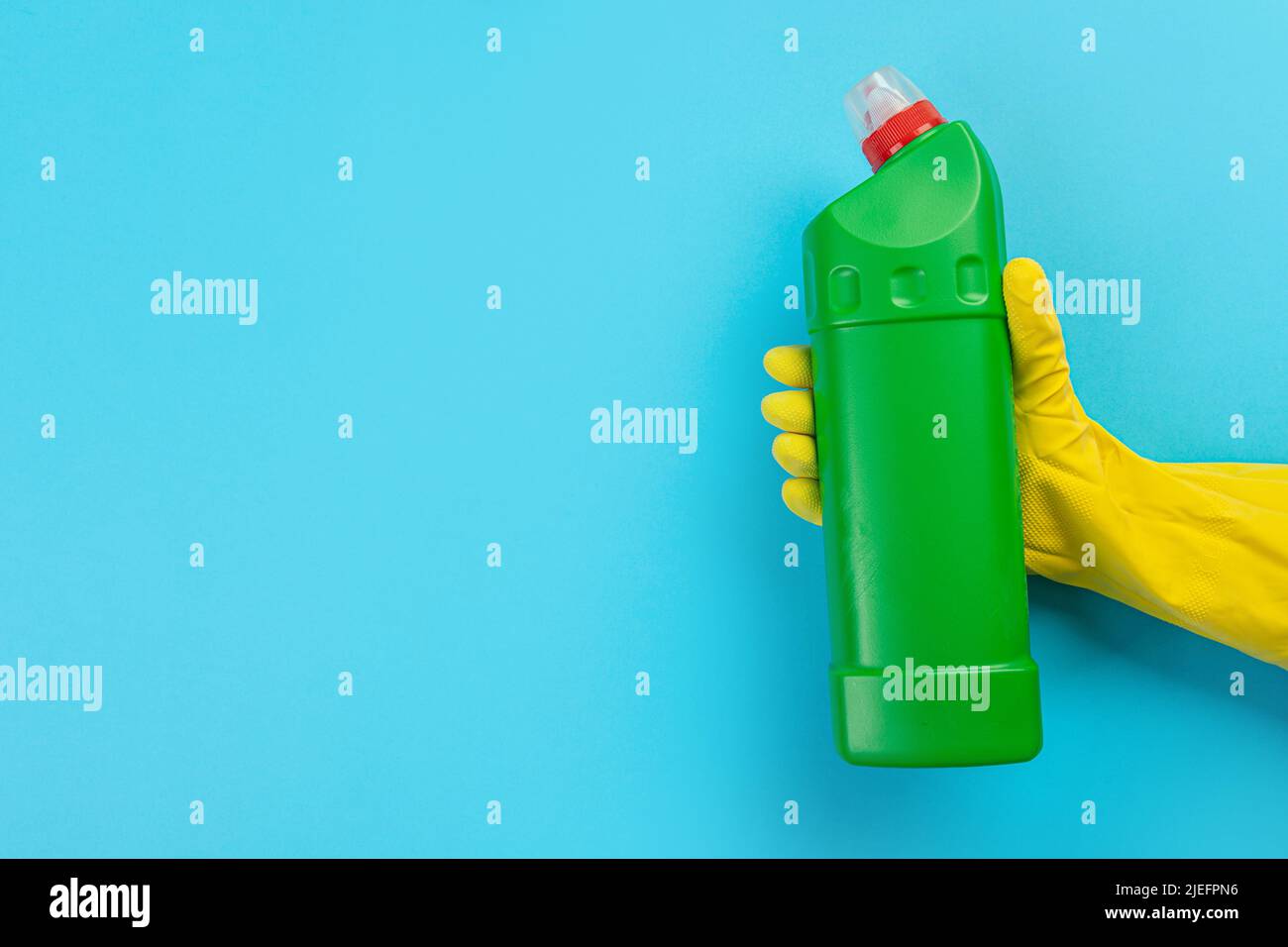 A hand in a rubber glove holds a green bottle of detergent on a blue ...