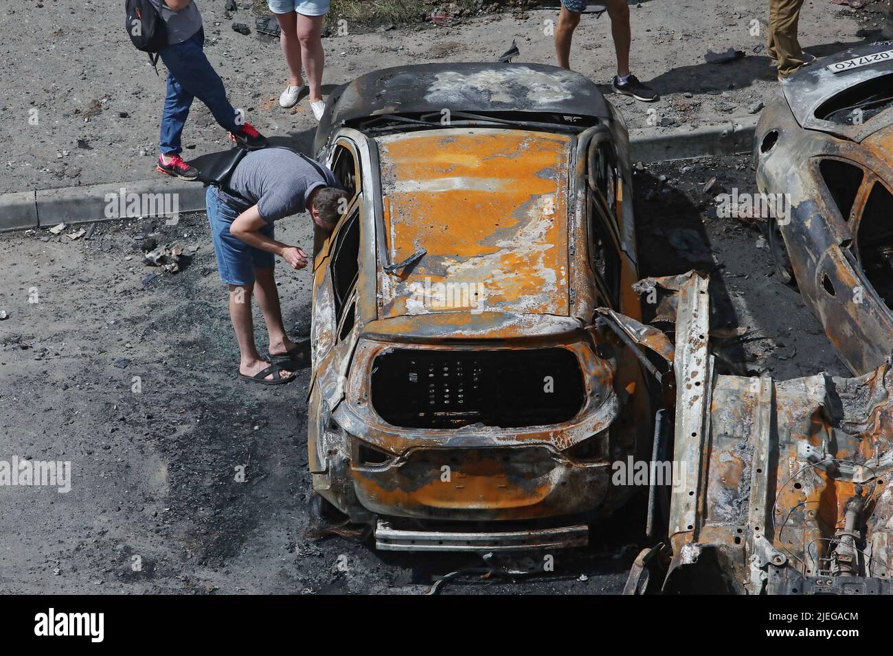 KHARKIV, UKRAINE - JUNE 26, 2022 - A man looks inside a burnt-out car in the yard of an apartment block after the Russian troops shelled a northern ne Stock Photo