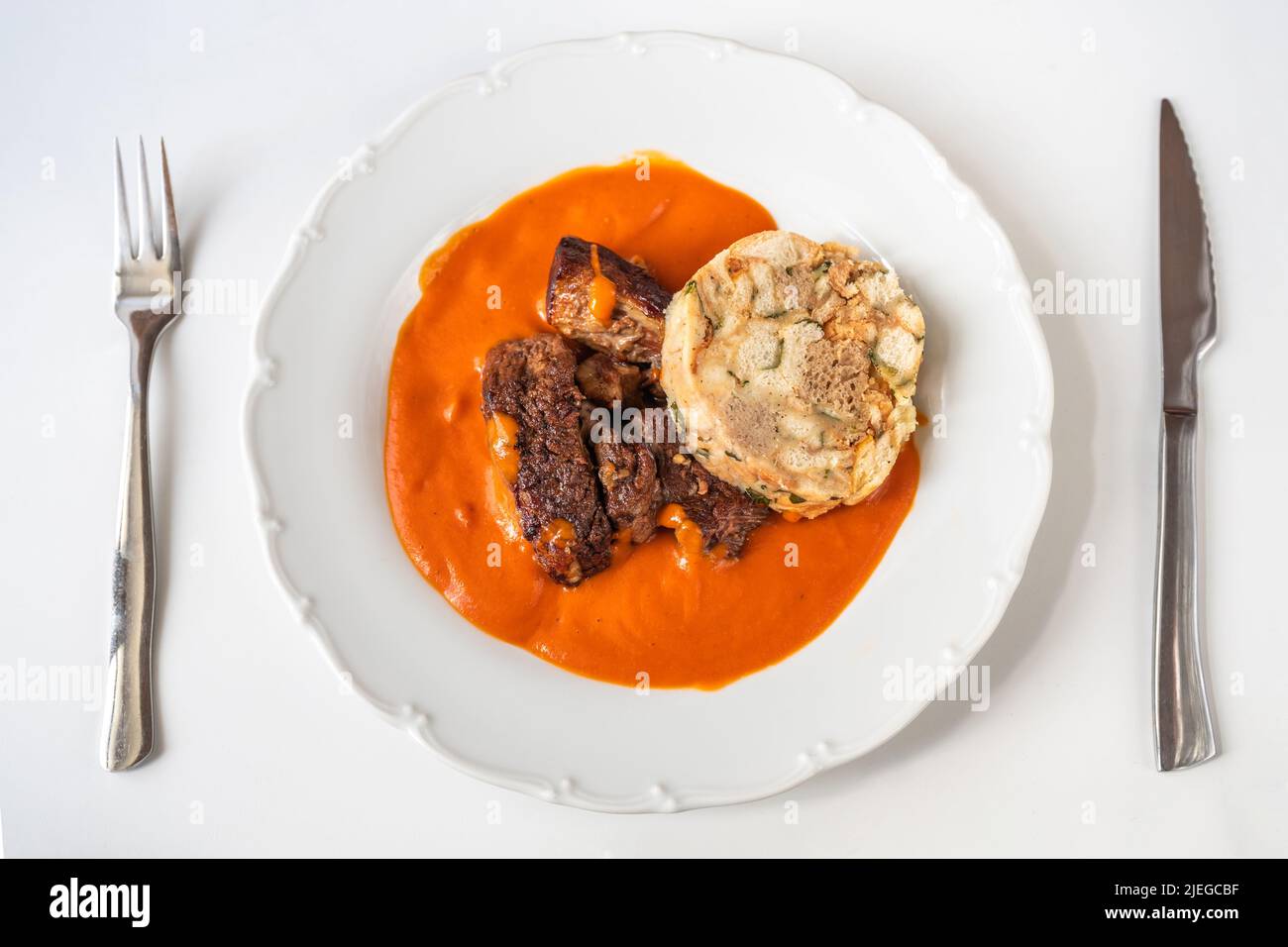 Tomato sauce, beef and dumpling in white plate, cutlery on white background. This meal is traditional and favourite in Czech republic. Stock Photo