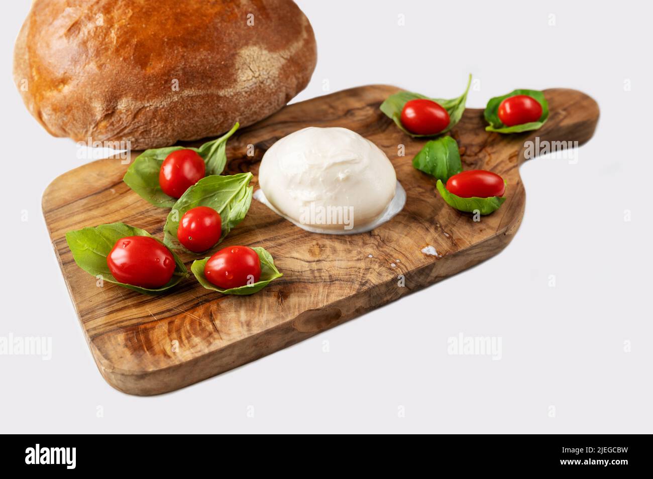 Cherry tomato on green basil leaf and mozzarella on wooden kitchen board, fresh bread loaf on white background, isolated,closeup. Stock Photo