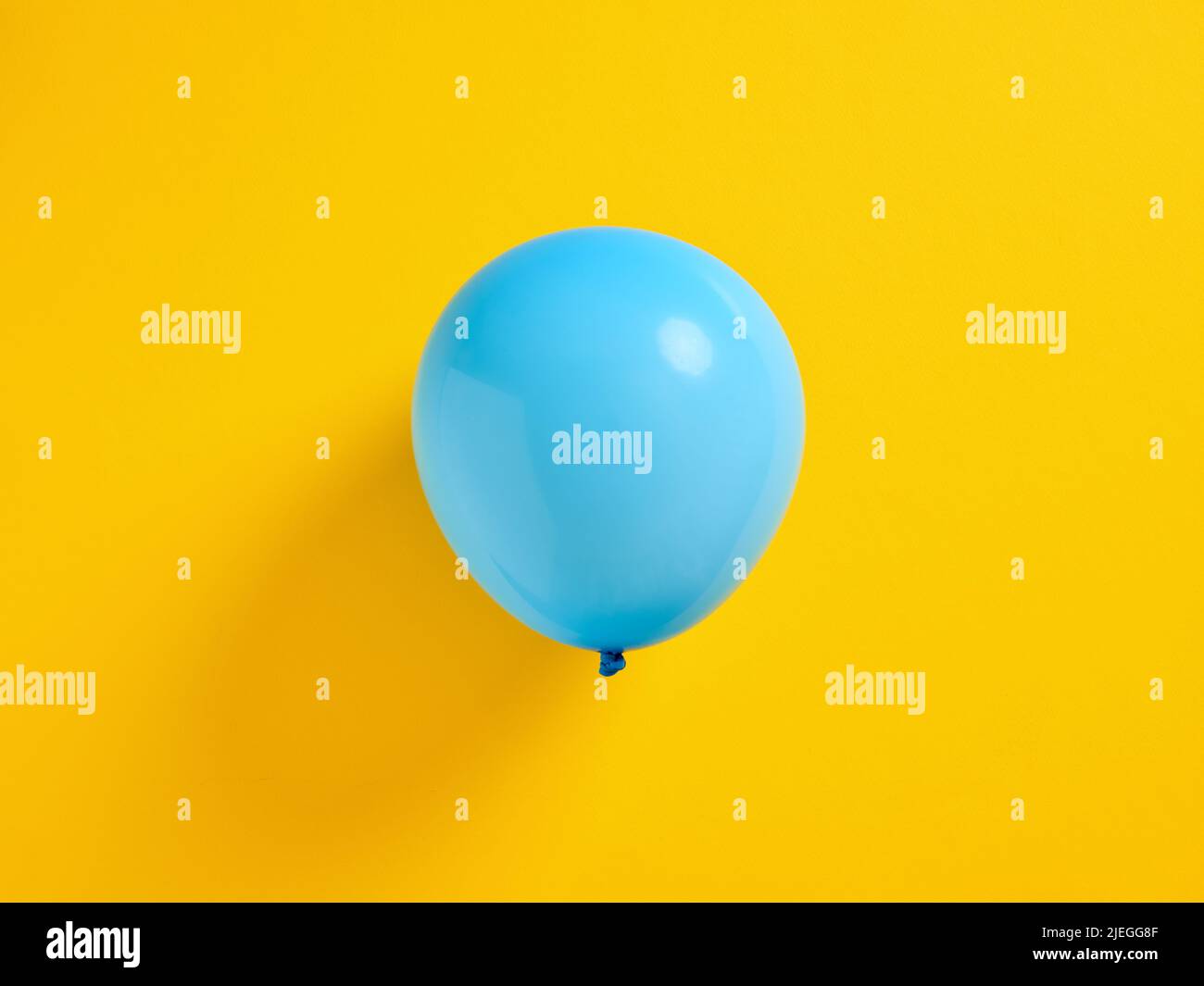 Blue inflated balloon on yellow background. Stock Photo
