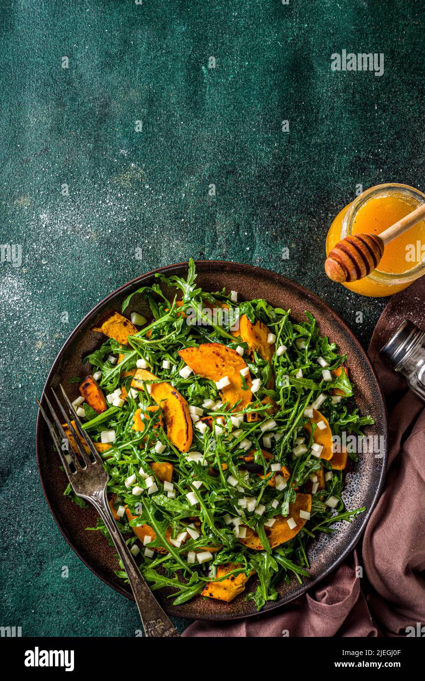 Homemade pumpkin salad with grilled pumpkin slices, arugula and cheese. Autumn pumpkin salad recipe, dark background copy space Stock Photo