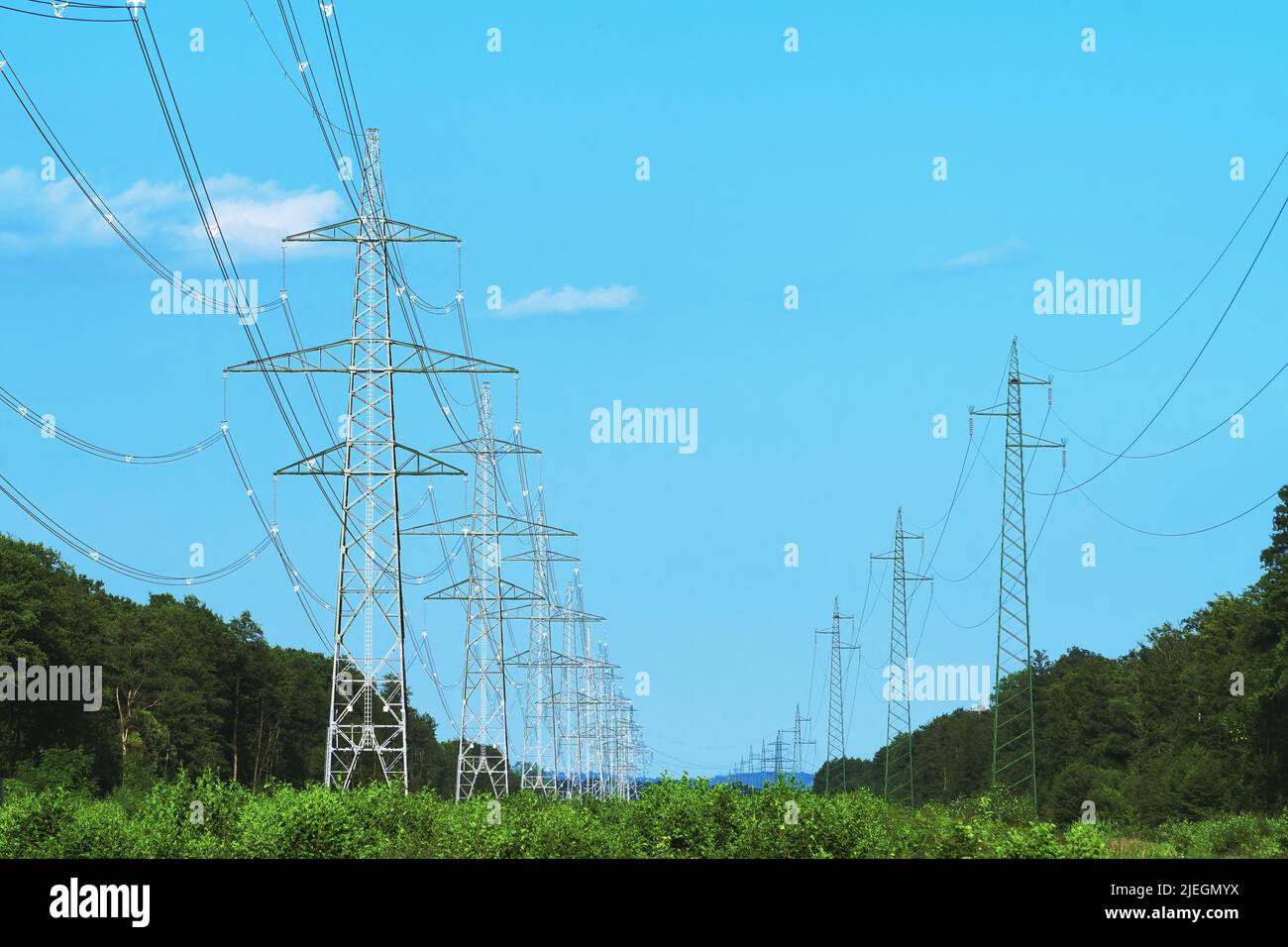 Long line of transmission towers on deforestated strip going through forest area. Electricity, power transmission and distribution, electrical energy, Stock Photo