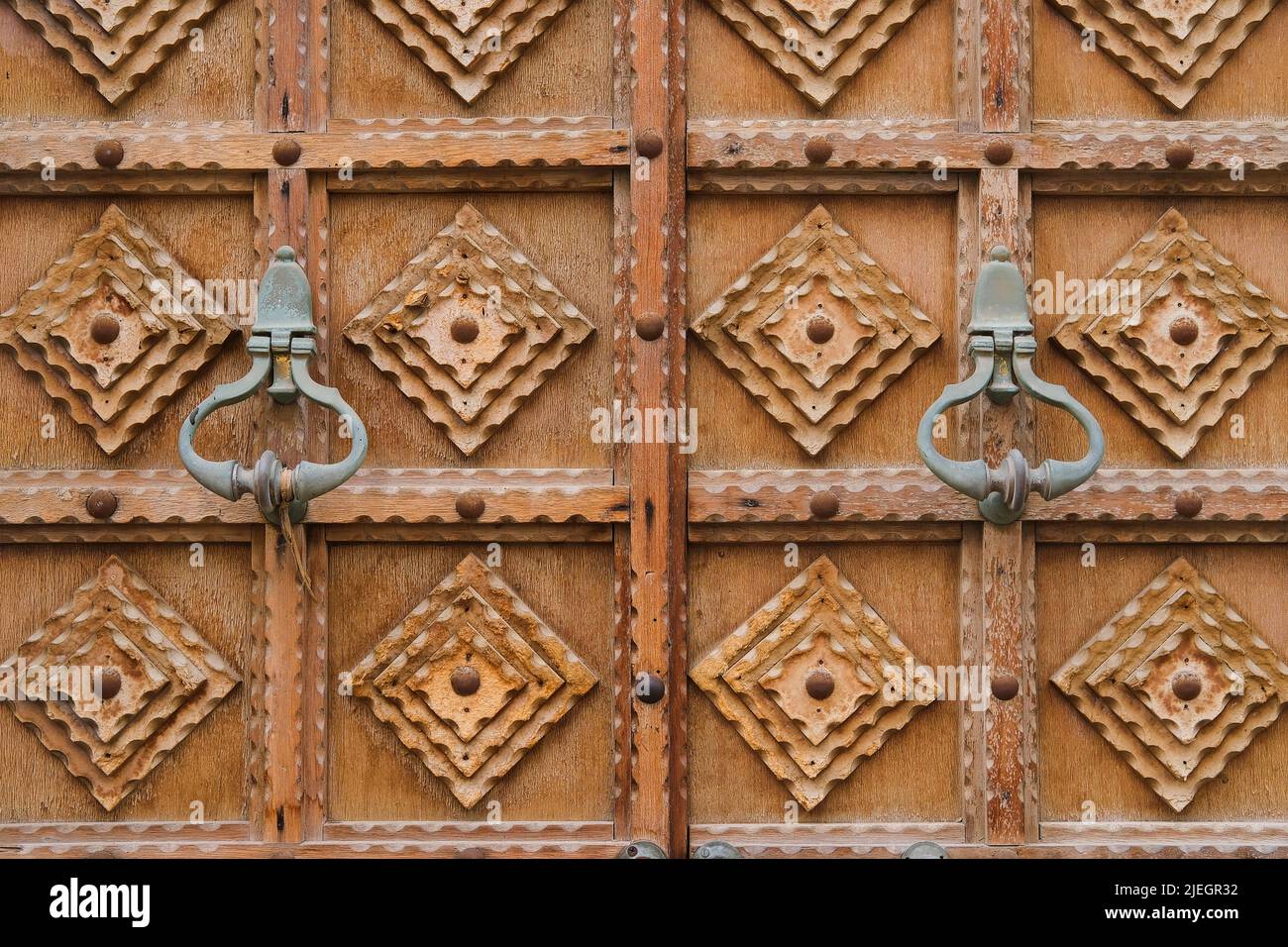 Minimalist wood carving design on timber gate. Fragment of vintage entrance door traditional carvings and patina handles Stock Photo