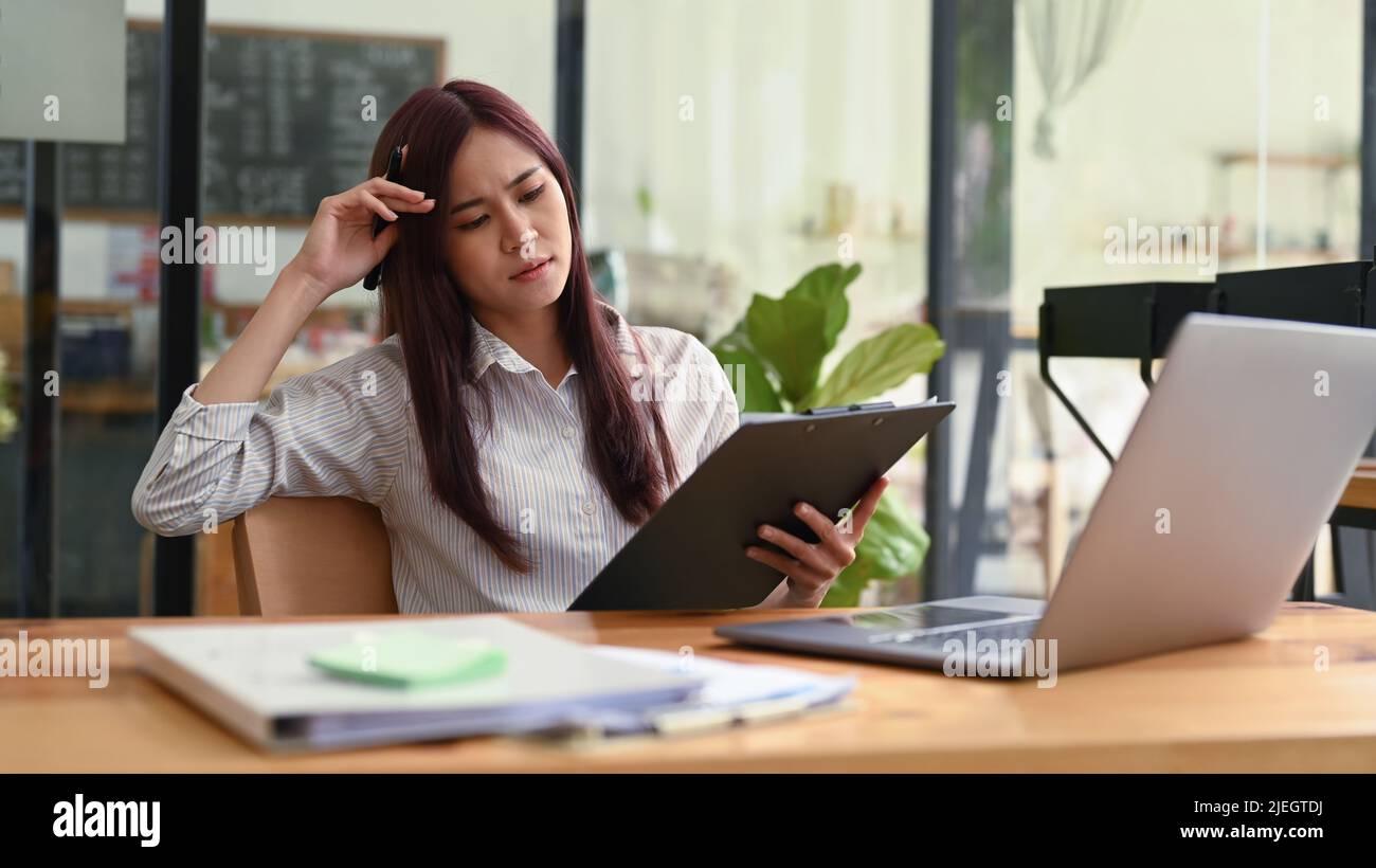 Serious young female employee sitting front of laptop and reading ...