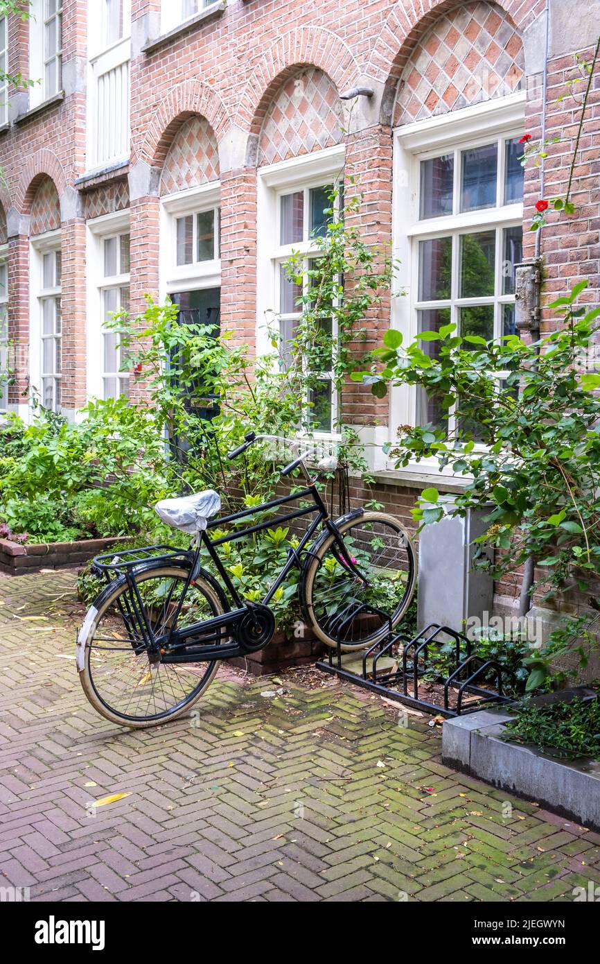 Bicycle parked in a bike stand front of a building, Amsterdam city neighborhood. Traditional red brick wall house, paved alley. Holland Netherlands Stock Photo