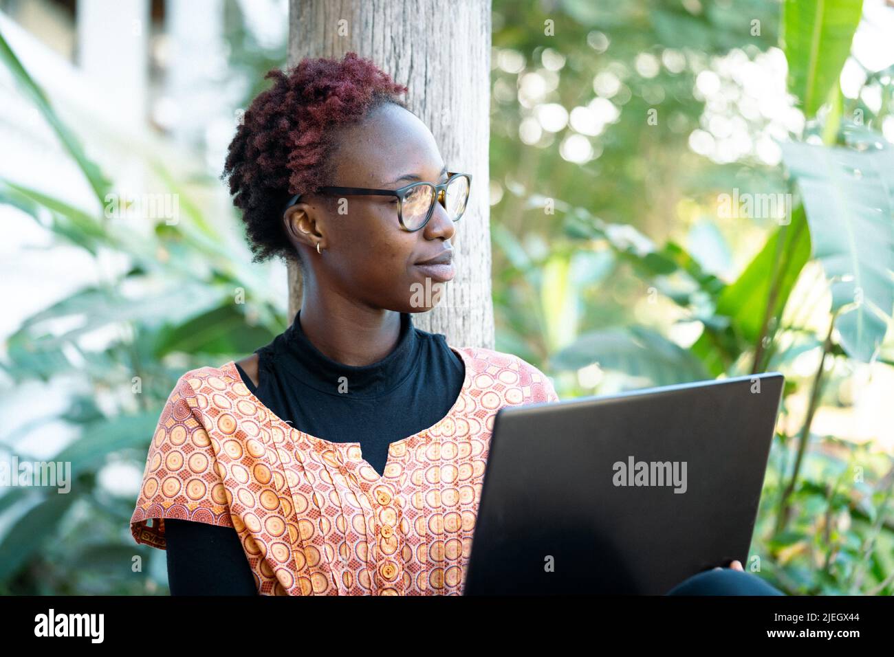 Young intellectual woman reading electronic book sitting in her garden with a dreamy look into the distance Stock Photo