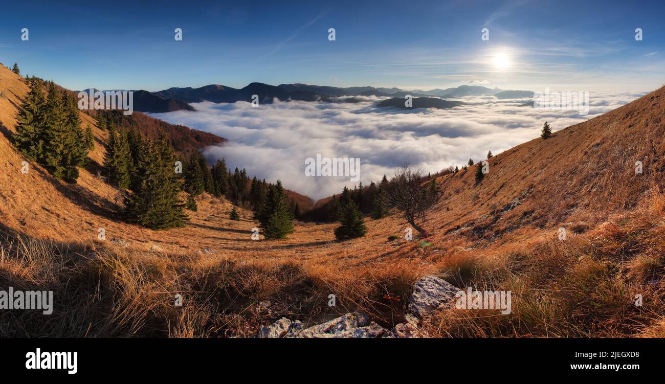 Panorama of the mountain landscape above clouds at sunset with sun Stock Photo