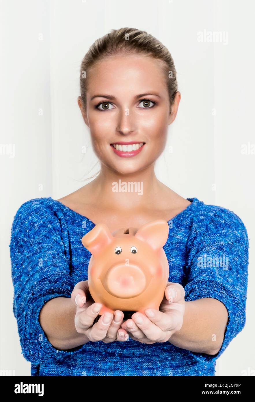 Eine junge Frau hält ein Sparschwein in ihrer Hand. Symbolfoto für Sparen, Geld anlegen und Altersvorsorge. Stock Photo