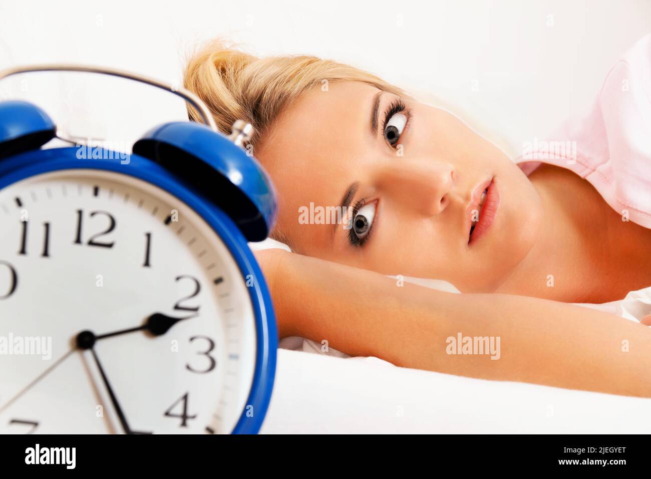 Schlaflosigkeit mit Uhr in der Nacht. Junge blonde Frau kann nicht schlafen, Wecker zeigt 2.25 Nachts, Stock Photo