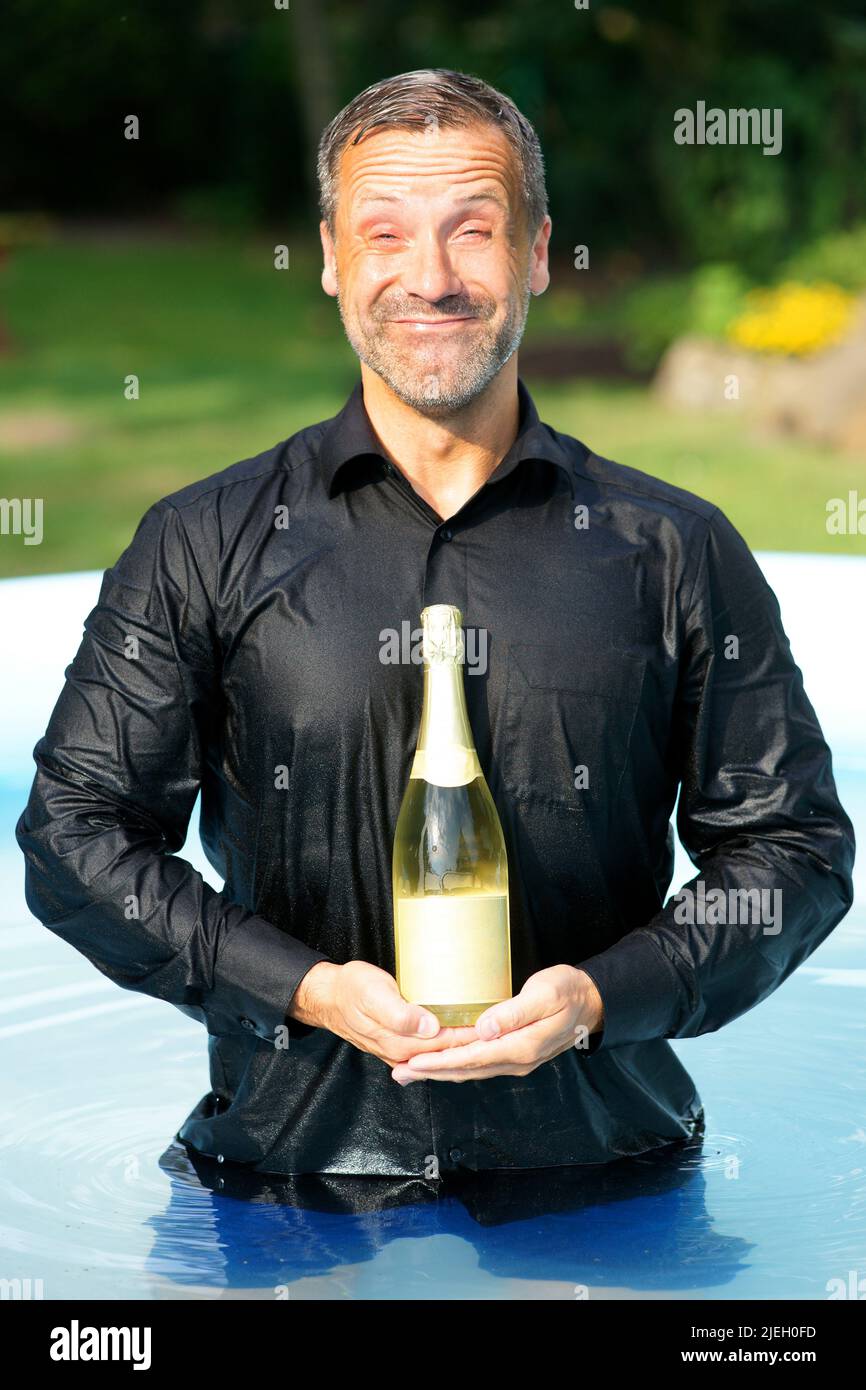 Ein Mann mit einer Flasche Sekt im Pool, Champagner , Feier, Übermütig, Stock Photo