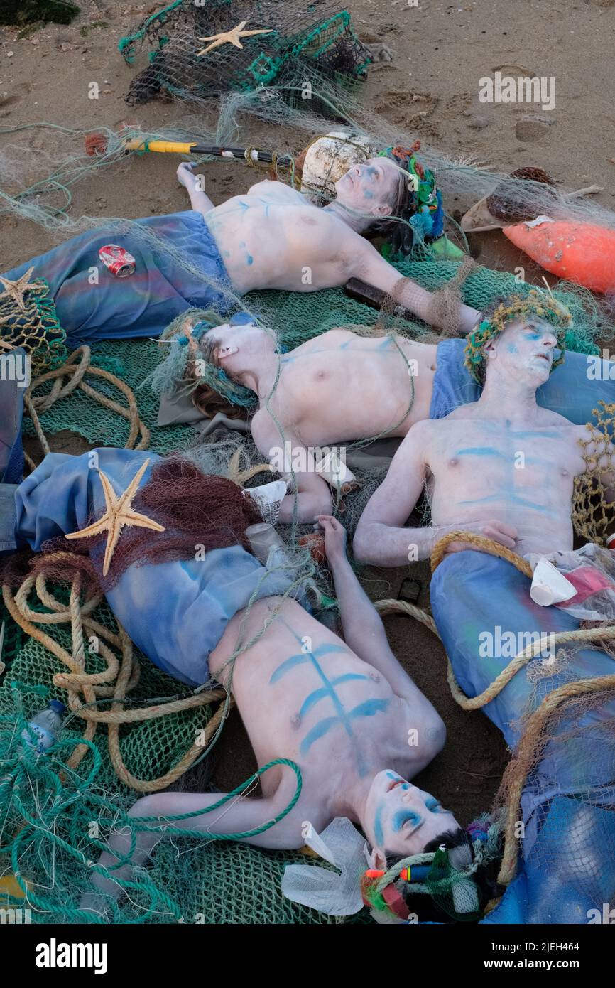 Lisbon, Portugal. 27th JUN 2022. Members of Ocean Rebellion perform a creative theatrical action where Dead Merfolk are washed-up at dawn, caught in a trawler-net along with debris from the sea (both plastics and seakill). Ocean Rebellion demands the UN calls for an end to all national fuel subsidies to fishing fleets and bans bottom trawling on the grounds of both needless biodiversity loss, through bycatch, and blue carbon release. Credit: Dan Pearson/Alamy Live News Stock Photo