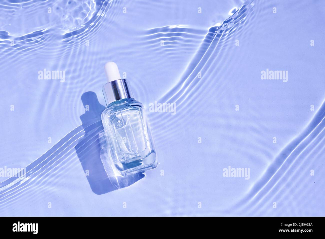 Cosmetic spa medical skin care, glass serum bottle, micellar tonic with collagen on blue water background with waves. Advertising medical serum for an Stock Photo