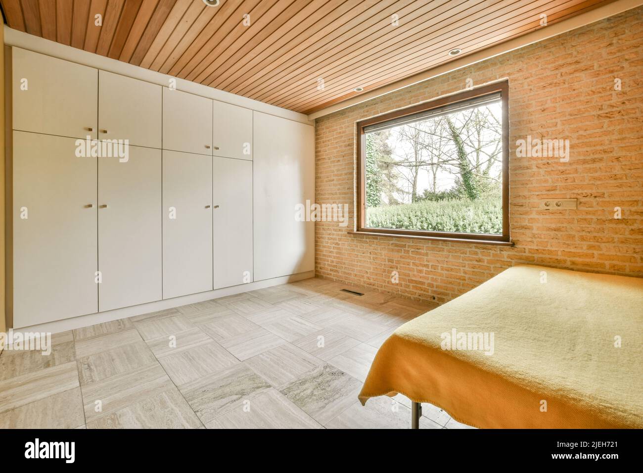 Comfortable bed with ornamental blanket placed near glass door and wardrobe with mirror in light bedroom Stock Photo