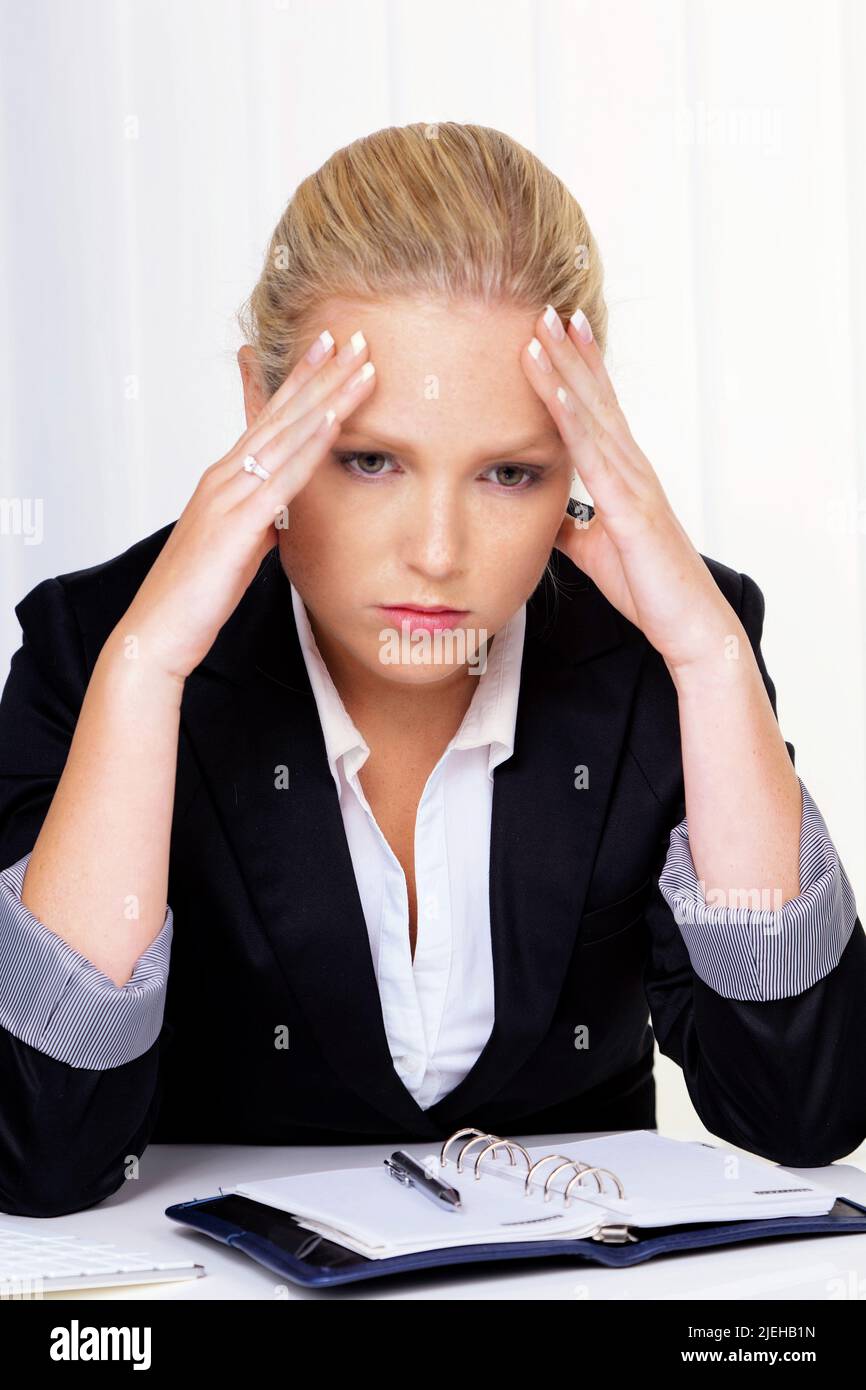 Eine junge Frau mit Migr‰ne und Kopfschmerzen sitzt in einem B¸ro. Stock Photo