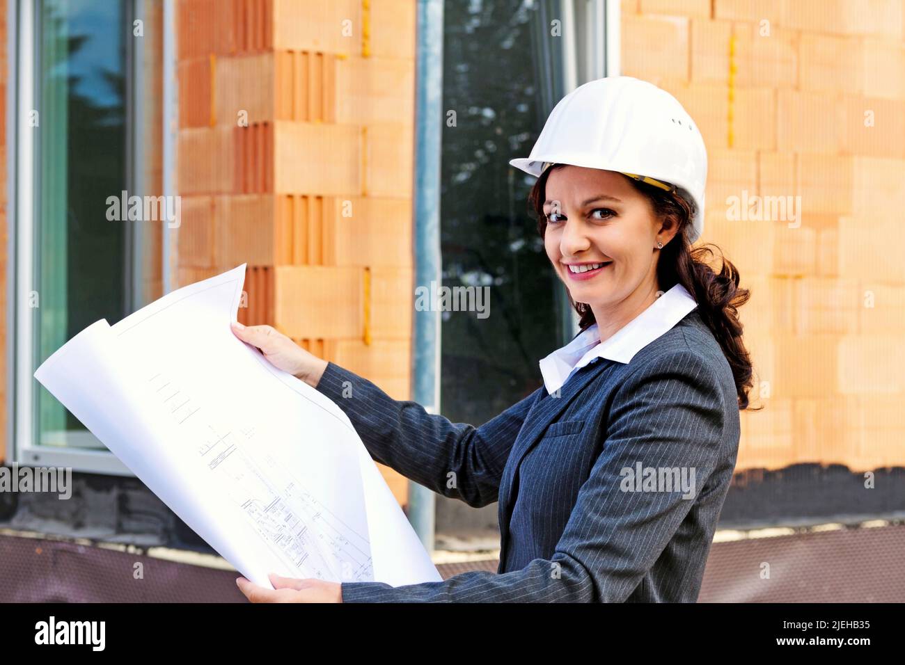 Junge Architektin mit Bauplan vor Rohbau eines Wohnhauses Stock Photo