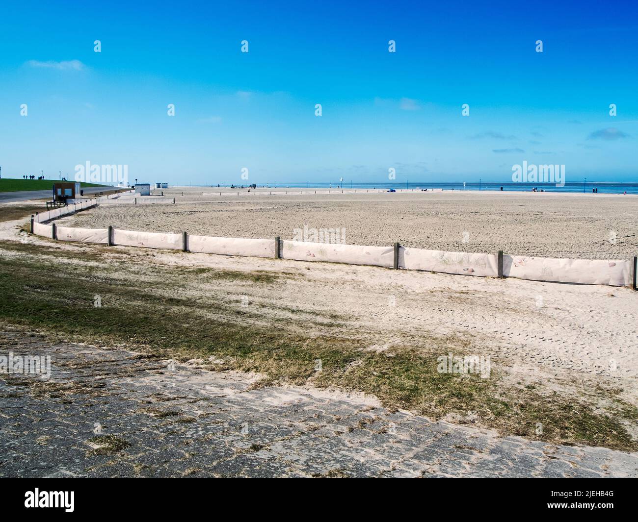 Landscape view of the smoothed bathing beach with fence near Neuharlingersiel in East Friesland in March 2022 with a blue sky. Stock Photo