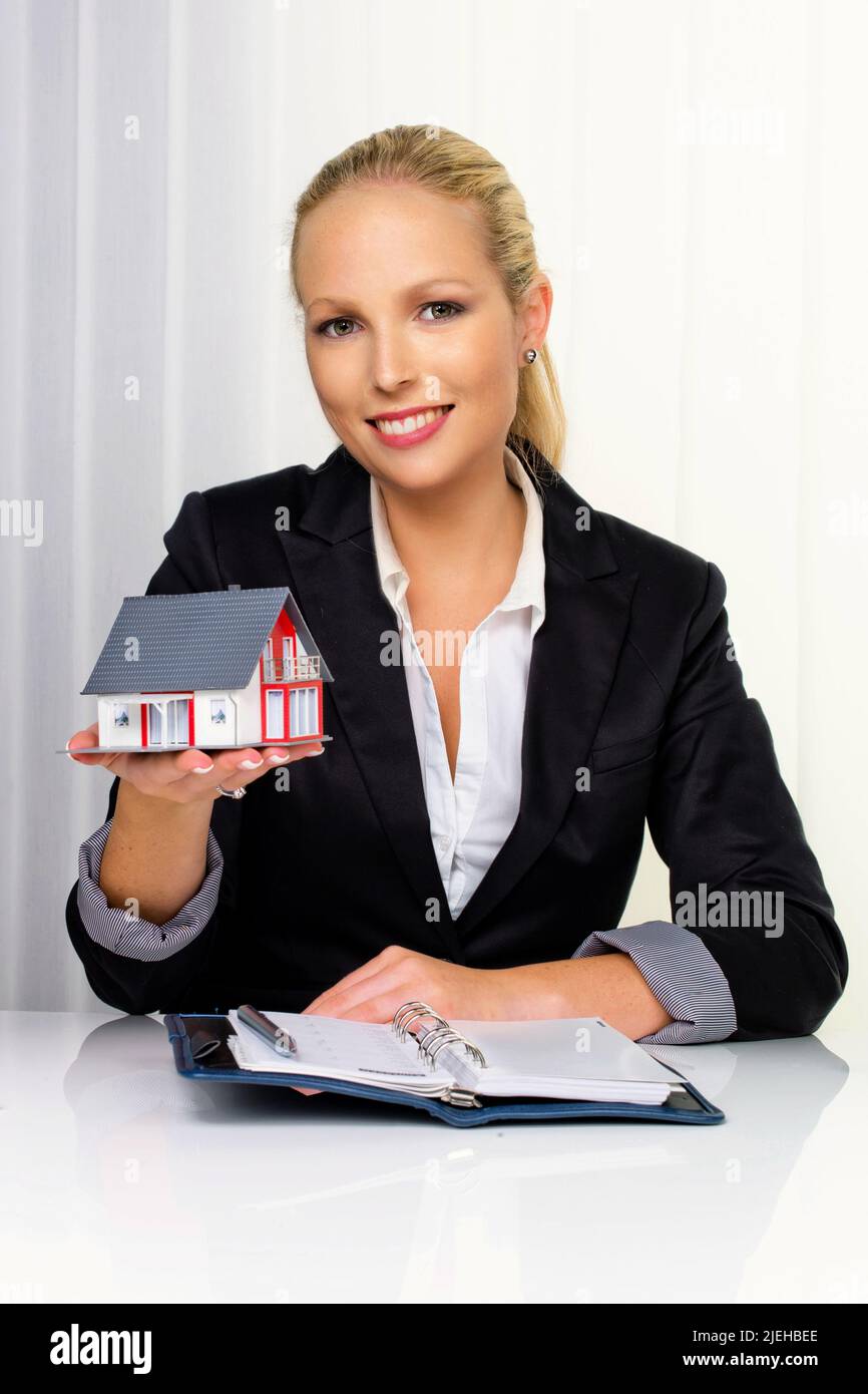 Eine junge Immobilien Maklerin mit einem Modellhaus in ihrem Büro. 30,35, Jahre, Blonde, Frau, Sommersprossen, Stock Photo