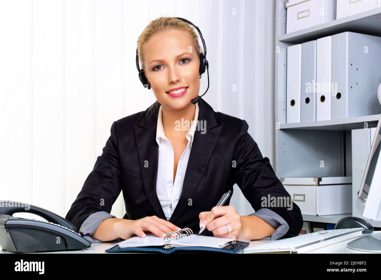 Eine freundliche junge Frau mit Headset im Kundendienstcenter telefoniert mit einem Kunden. Freundliche Hotline, Mitarbeiterin, Call Center, Sekretäri Stock Photo