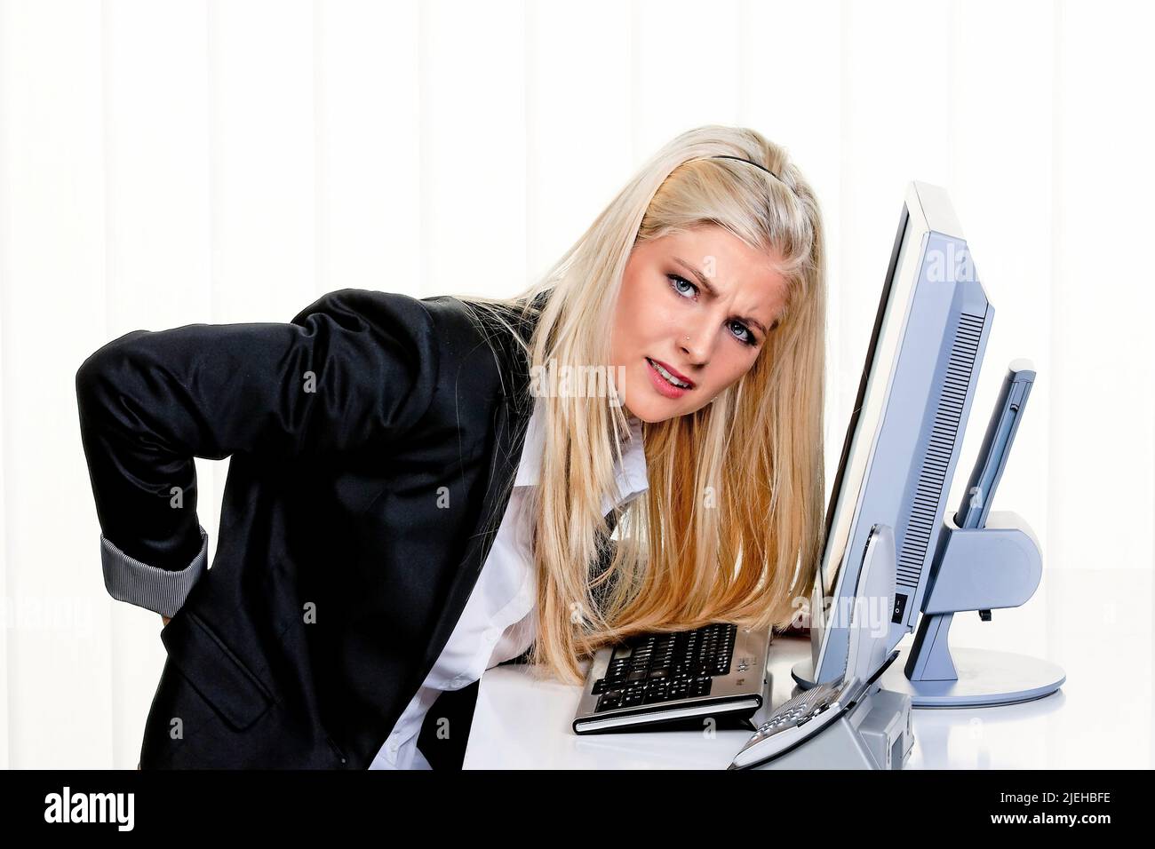 Eine junge Frau sitzt im Büro und hat Rückenschmerzen Stock Photo