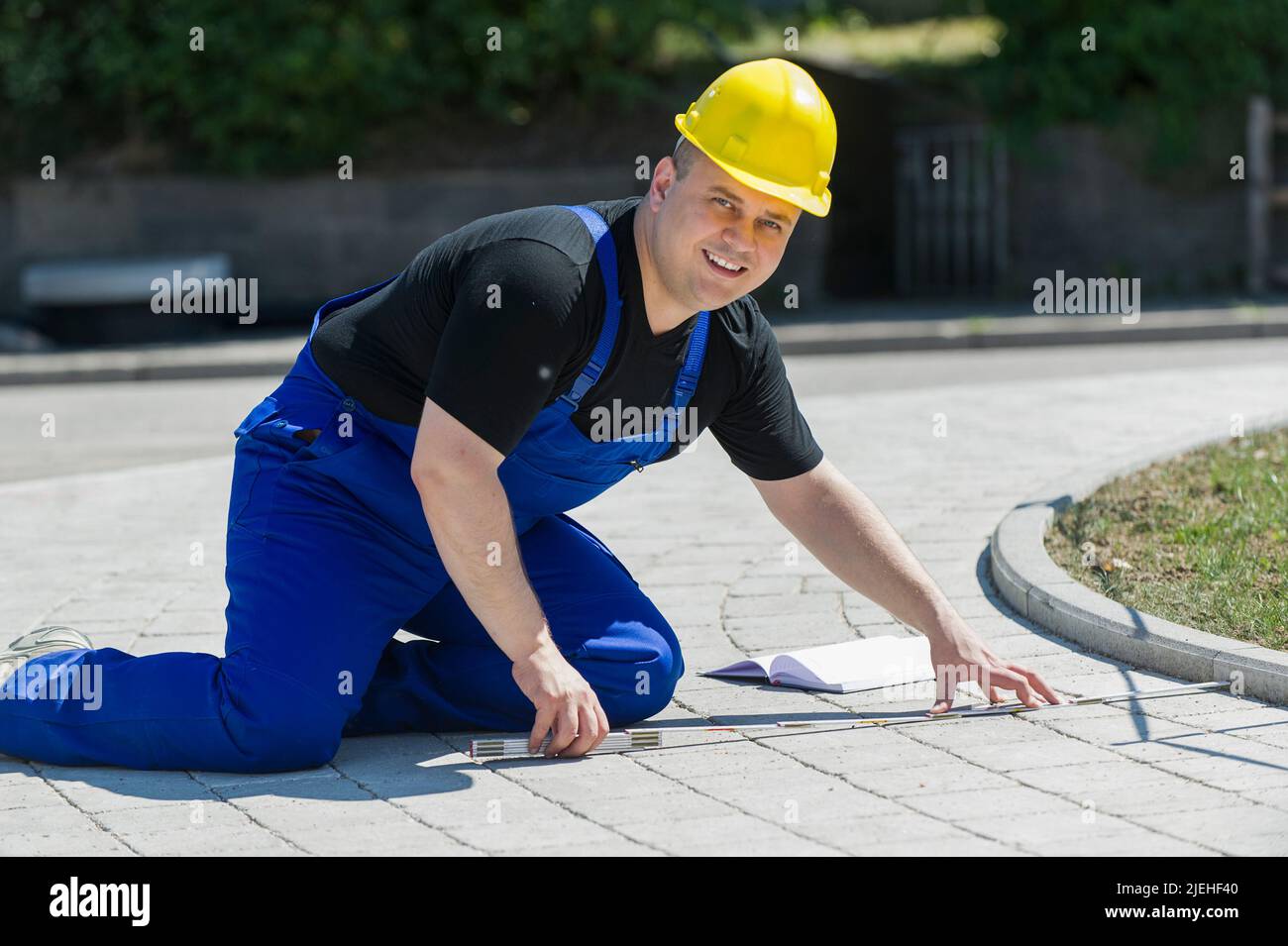 Ein Bauarbeiter mit Zollstock in der Hand vermisst einen gepflasterten Weg, gelber Schutzhelm, Bauarbeiter, Beruf, Berufe, Stock Photo