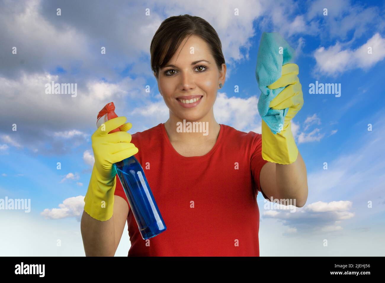 Junge Frau mit Reinigungsmittel putzt eine Fensterscheibe von aussen, durcvh die Scheibe fotografiert, blauer Himmel, Stock Photo