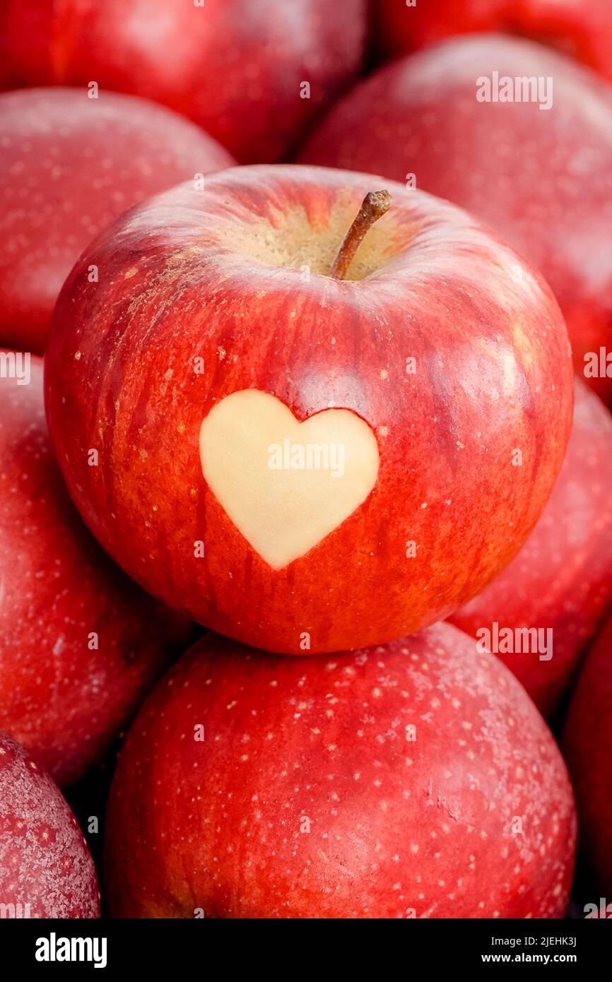 Roter Apfel mit Herz liegt auf roten Äpfeln, Stock Photo