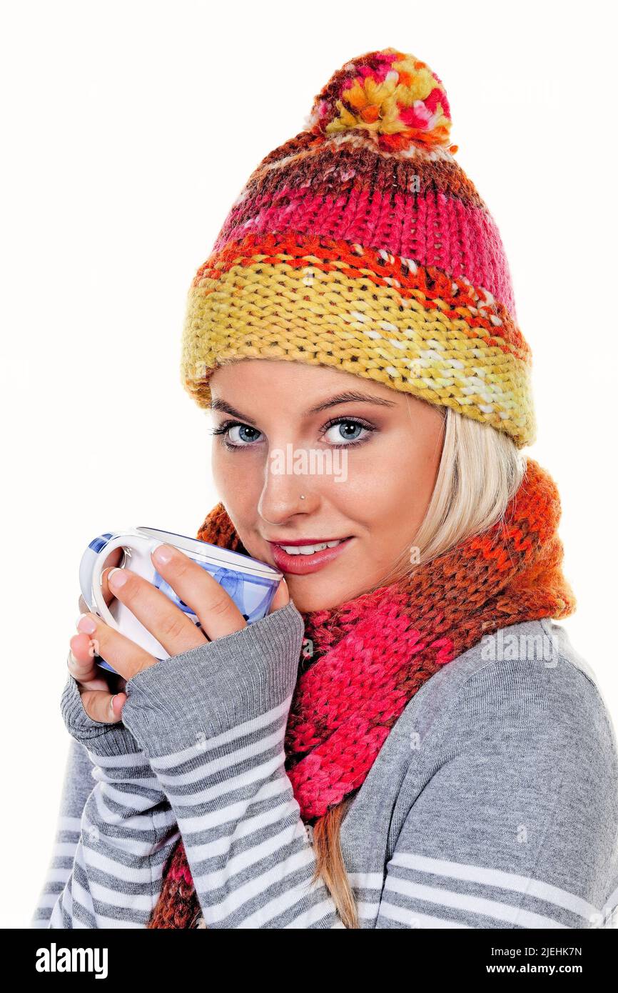 Eine junge blonde Frau mit Schal und Mütze trinkt einen Kaffee im Winter, Aufwärmen, Getränk, Pudelmütze, Kaffeebecher, Stock Photo