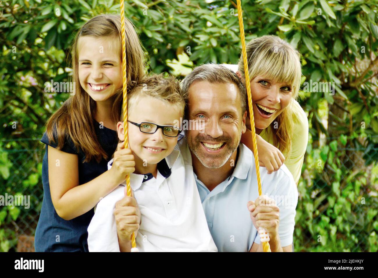 Vater und Mutter sowie zwei Kinder schaukeln im Garten Stock Photo