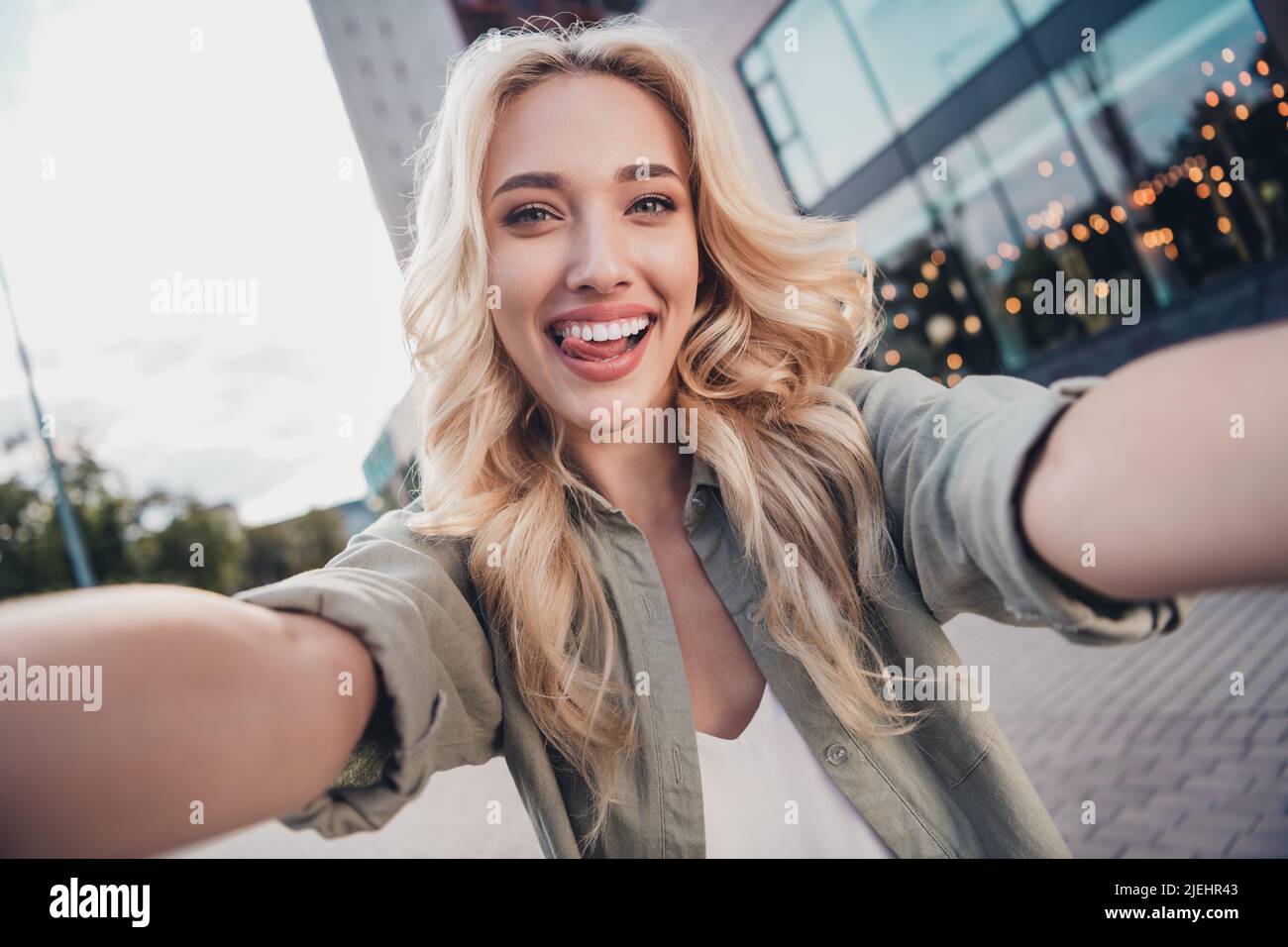 Self portrait of attractive cheerful funky wavy haired girl traveling showing tongue out fooling in town outdoors Stock Photo