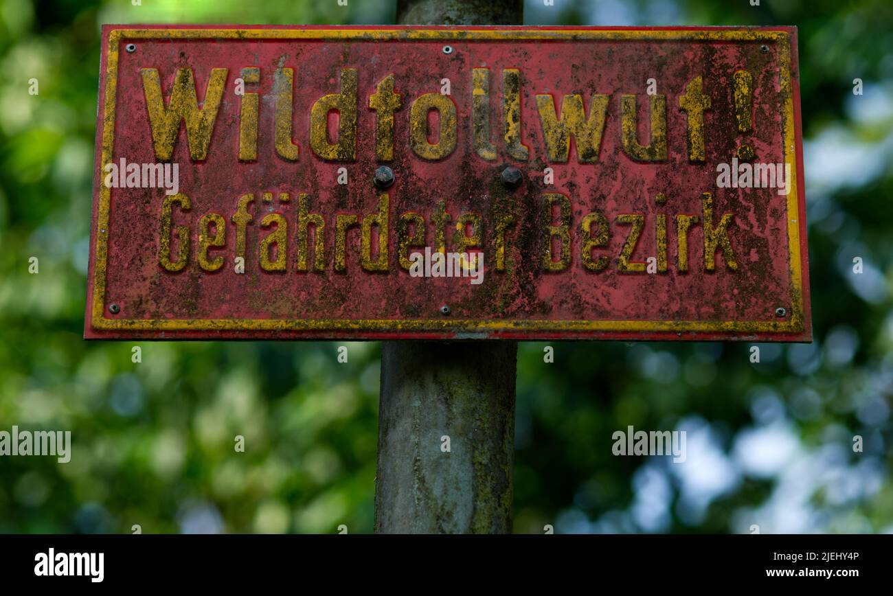 old weathered red warning sign lettering 'Wildtollwut! - gefährdeter Bezirk' (German for 'Rabies of wild animals! Endangered district') Stock Photo