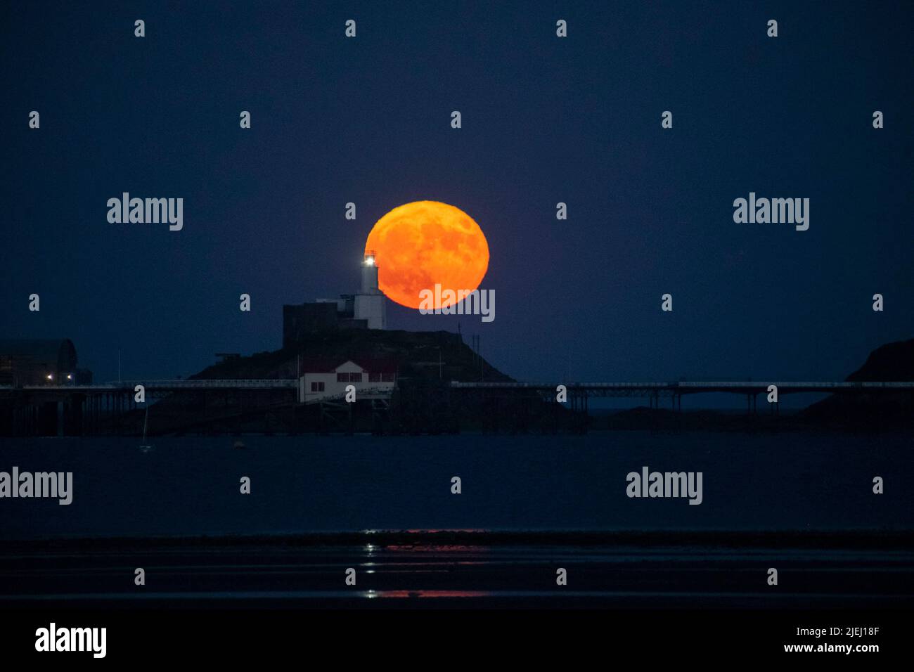 The Strawberry Full Moon pictured behind Mumbles Head in Swansea, Wales, as the Supermoon rises into the evening sky. It is the sixth full moon of the year, but the as it is a supermoon, it appears larger and brighter in the evening sky. Stock Photo