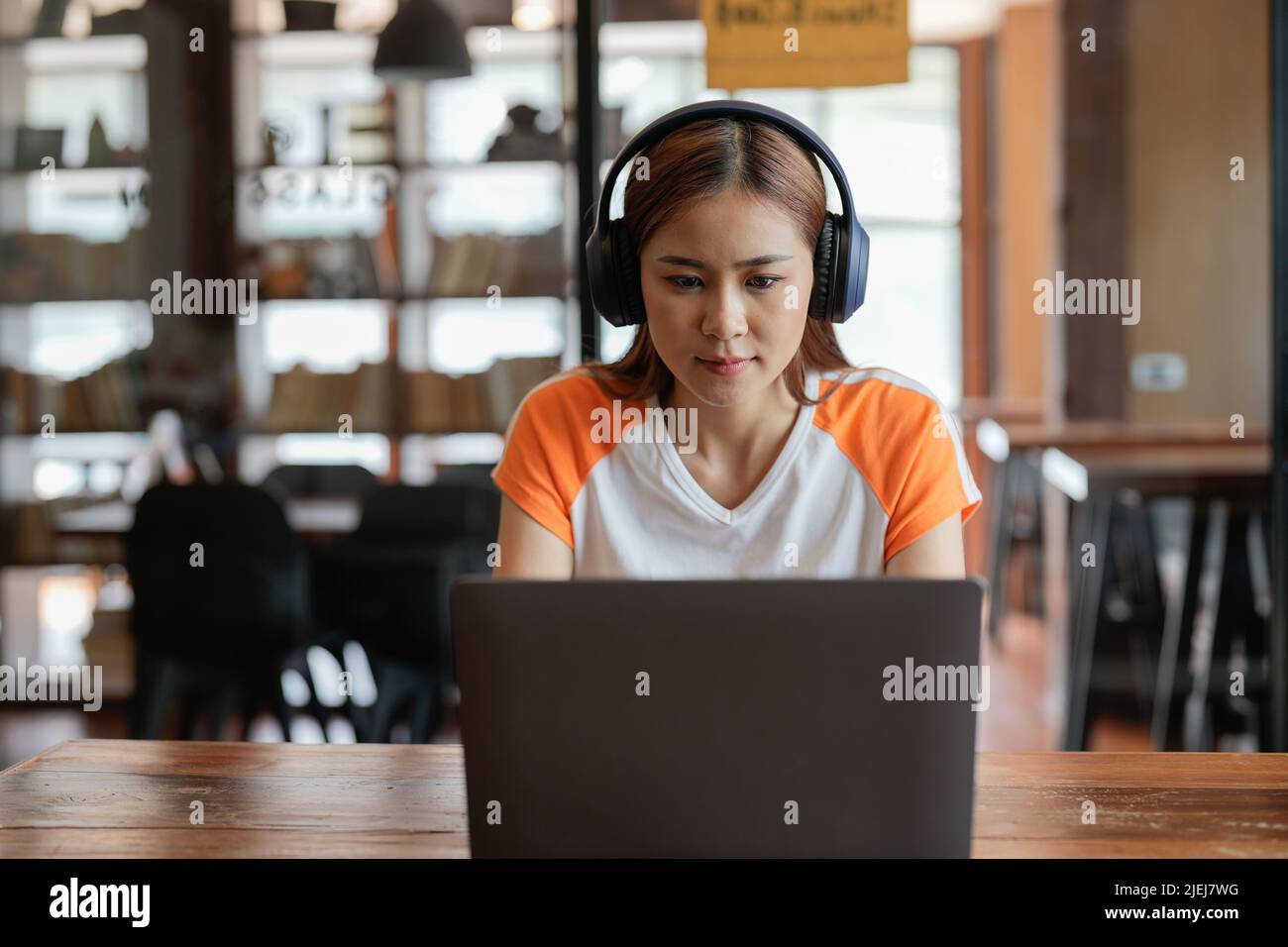 Seriously teenage asian female remote student sit by home computer participate at virtual event distant lesson. Confident young biracial woman in Stock Photo