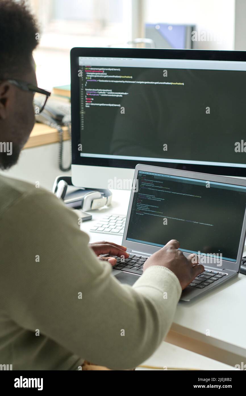 Rear view of young programmer sitting at table and typing on laptop, he working with codes to develop new software Stock Photo