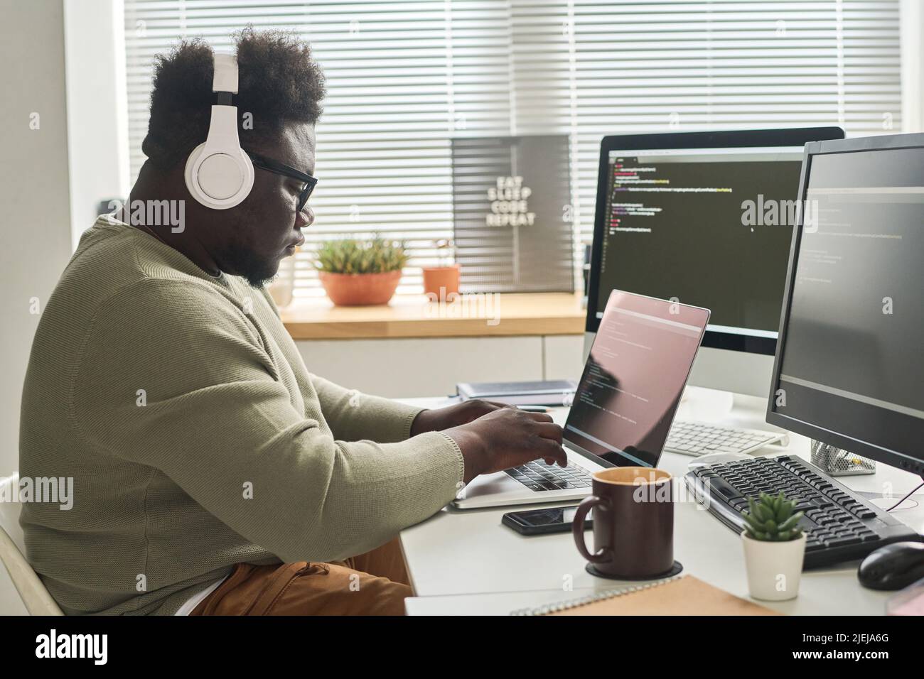 African IT programmer in wireless headphone concentrating on his online work on laptop, he writing computer codes to program Stock Photo