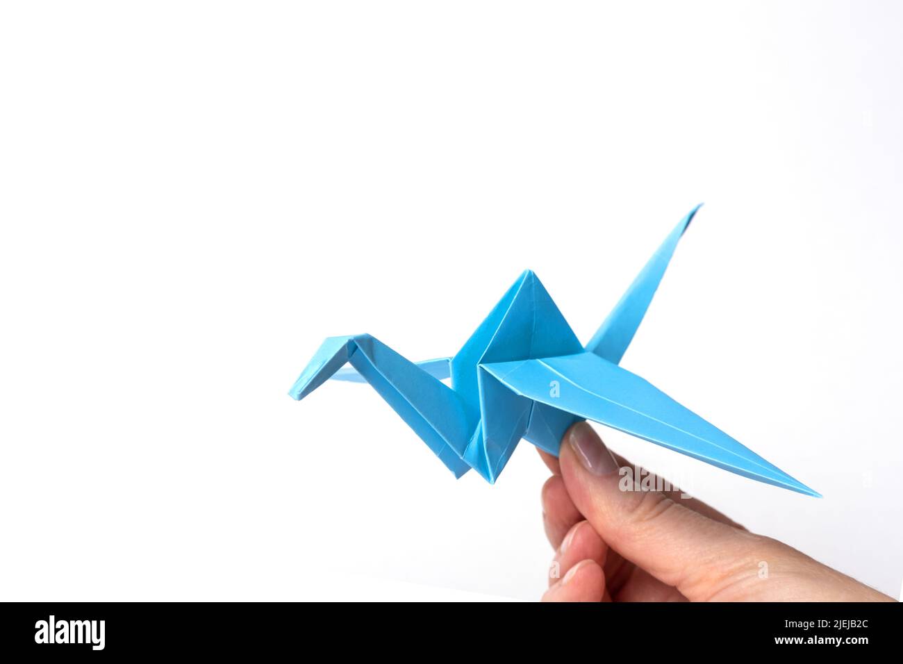 Hand holding paper blue bird isolated on white background. Paper crane as a symbol of peace. Paper origami. Paper crafts with children. Stock Photo