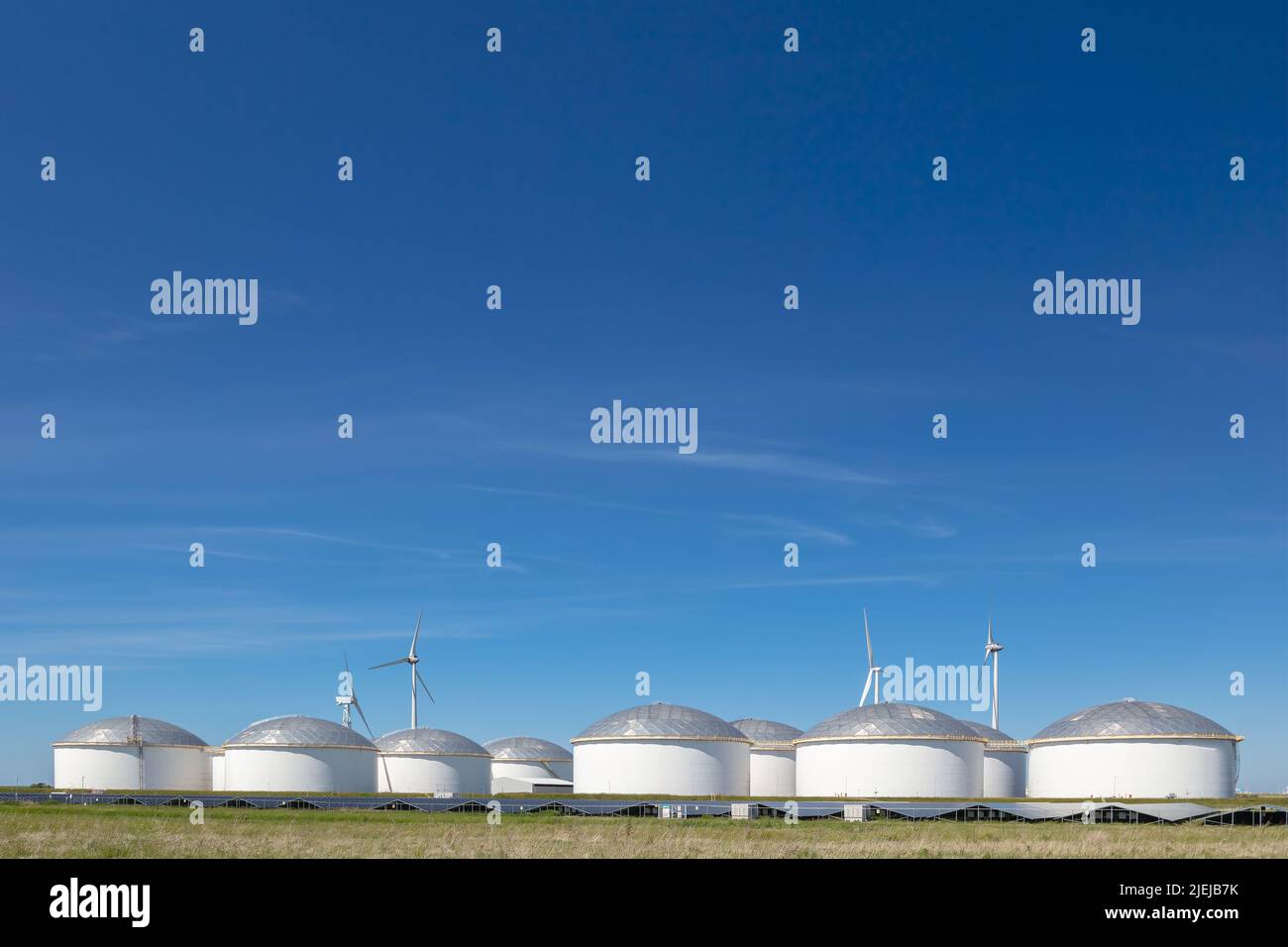 Large Dutch gas and fuel storage tanks with wind turbines and solar panels in front in the Eemshaven, The Netherlands Stock Photo