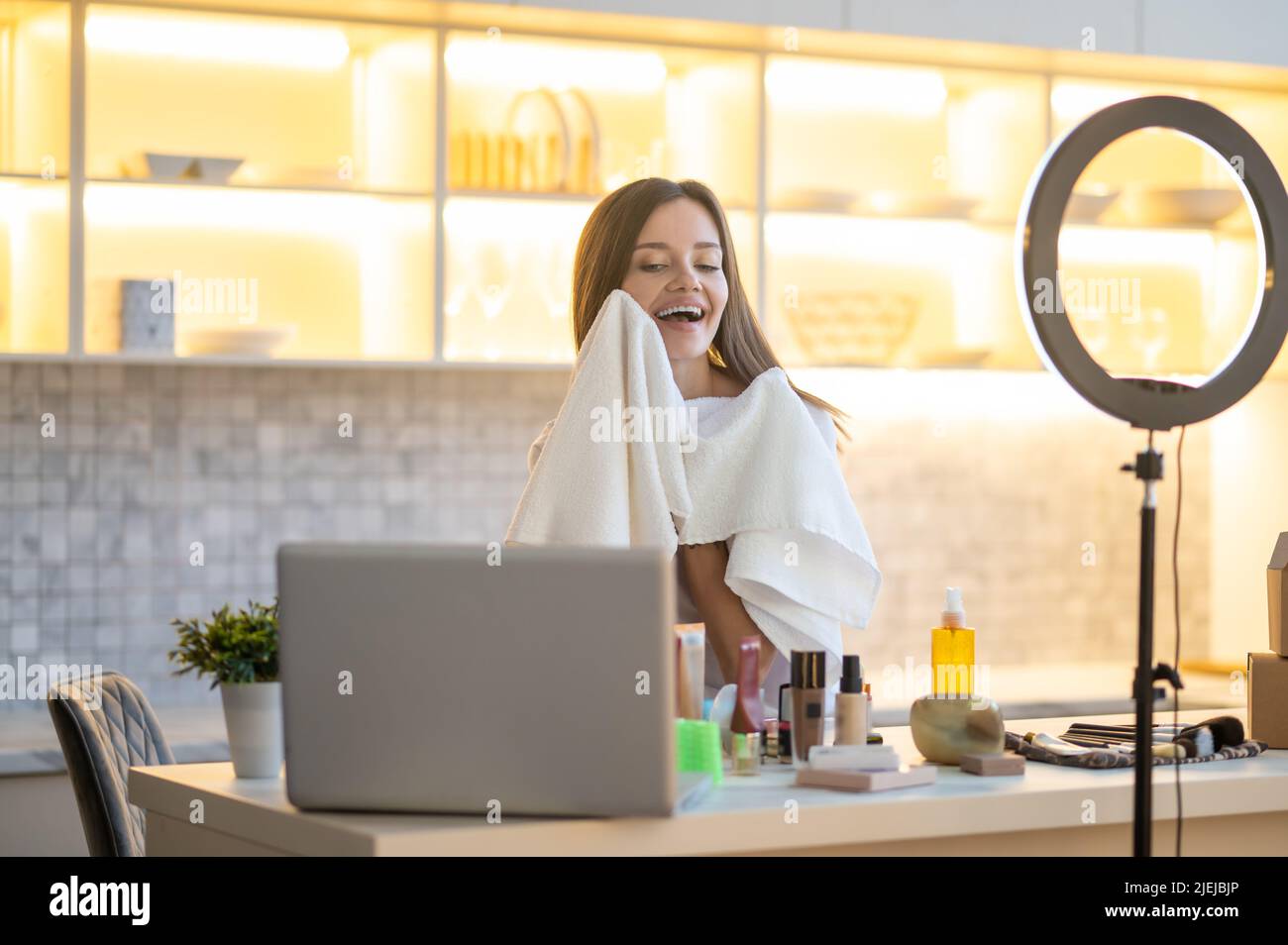 Woman touching cheek with towel while looking at laptop Stock Photo