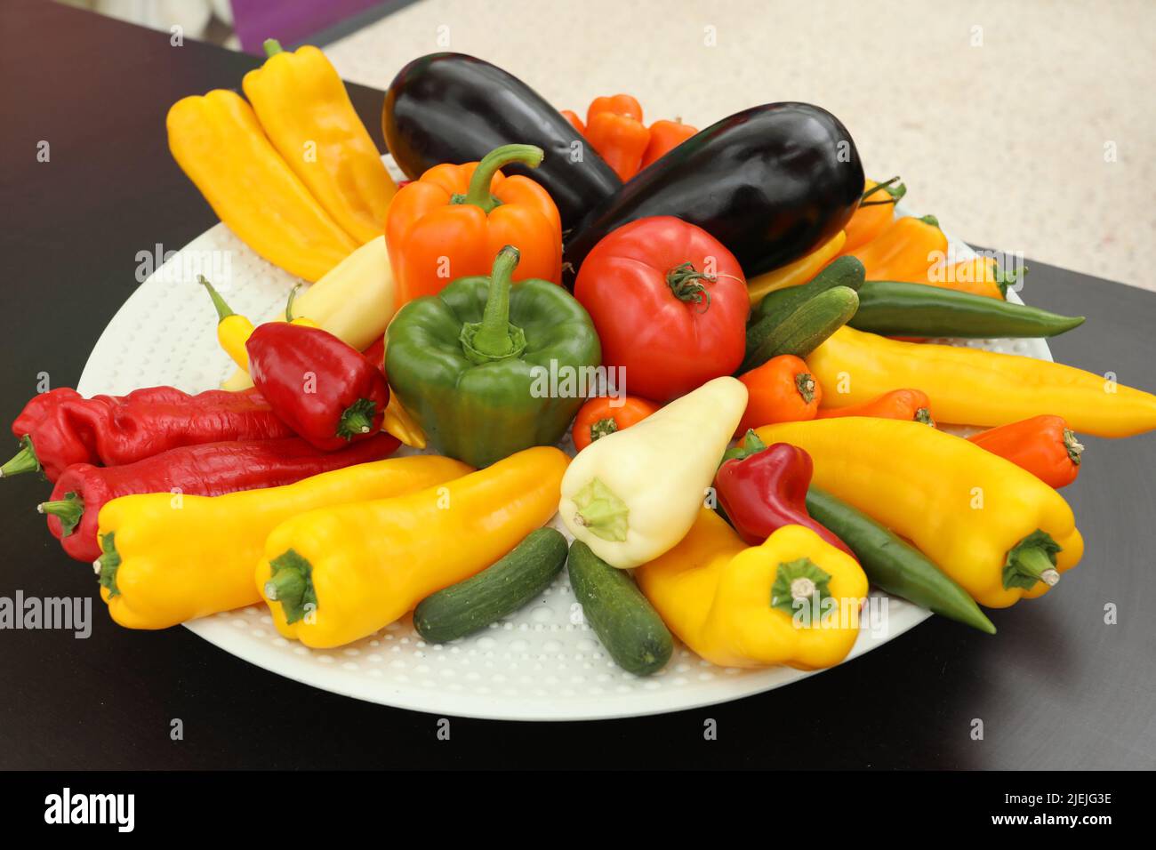 White plate of veggies with Bell peppers, yellow pepper, aubergine on a black table Stock Photo