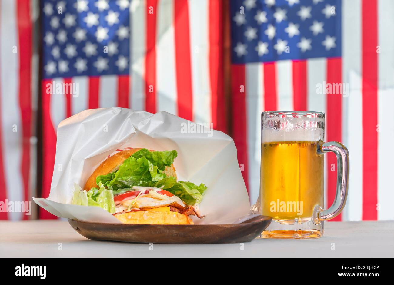 Delicious Sasebo burger with juicy patty and lettuce in sesame seed buns served on a wooden plate with a pint of lager against national flag of the un Stock Photo