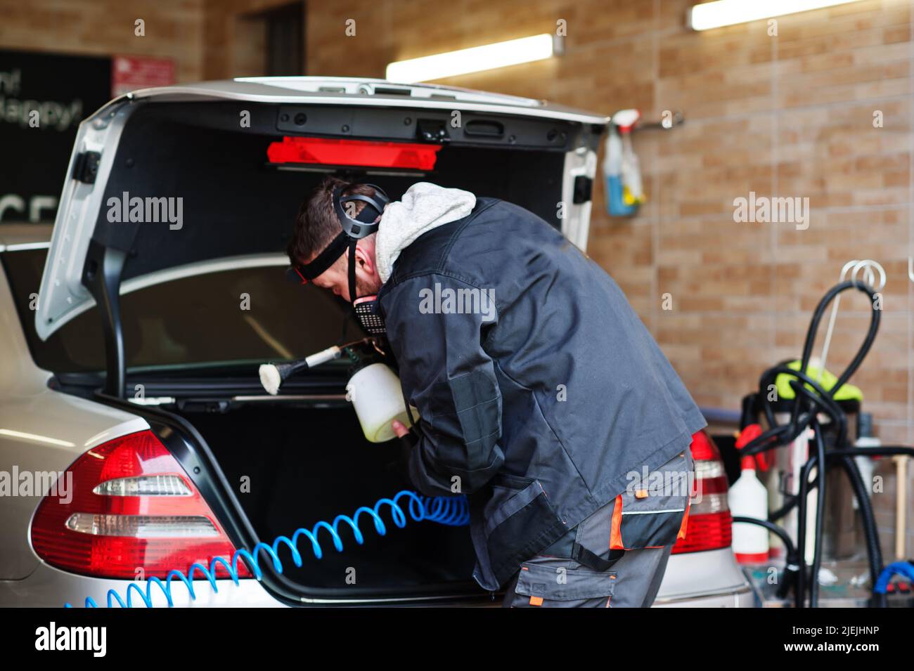 Man in uniform and respirator, worker of car wash center, cleaning car