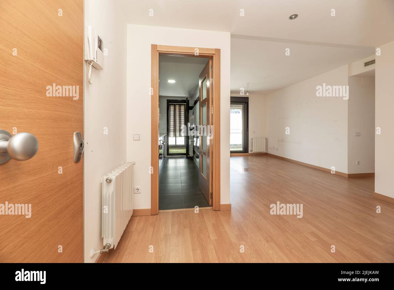 Entrance hall of a house with access to an empty living room with oak flooring and a kitchen with stoneware floors and a wooden and glass door Stock Photo