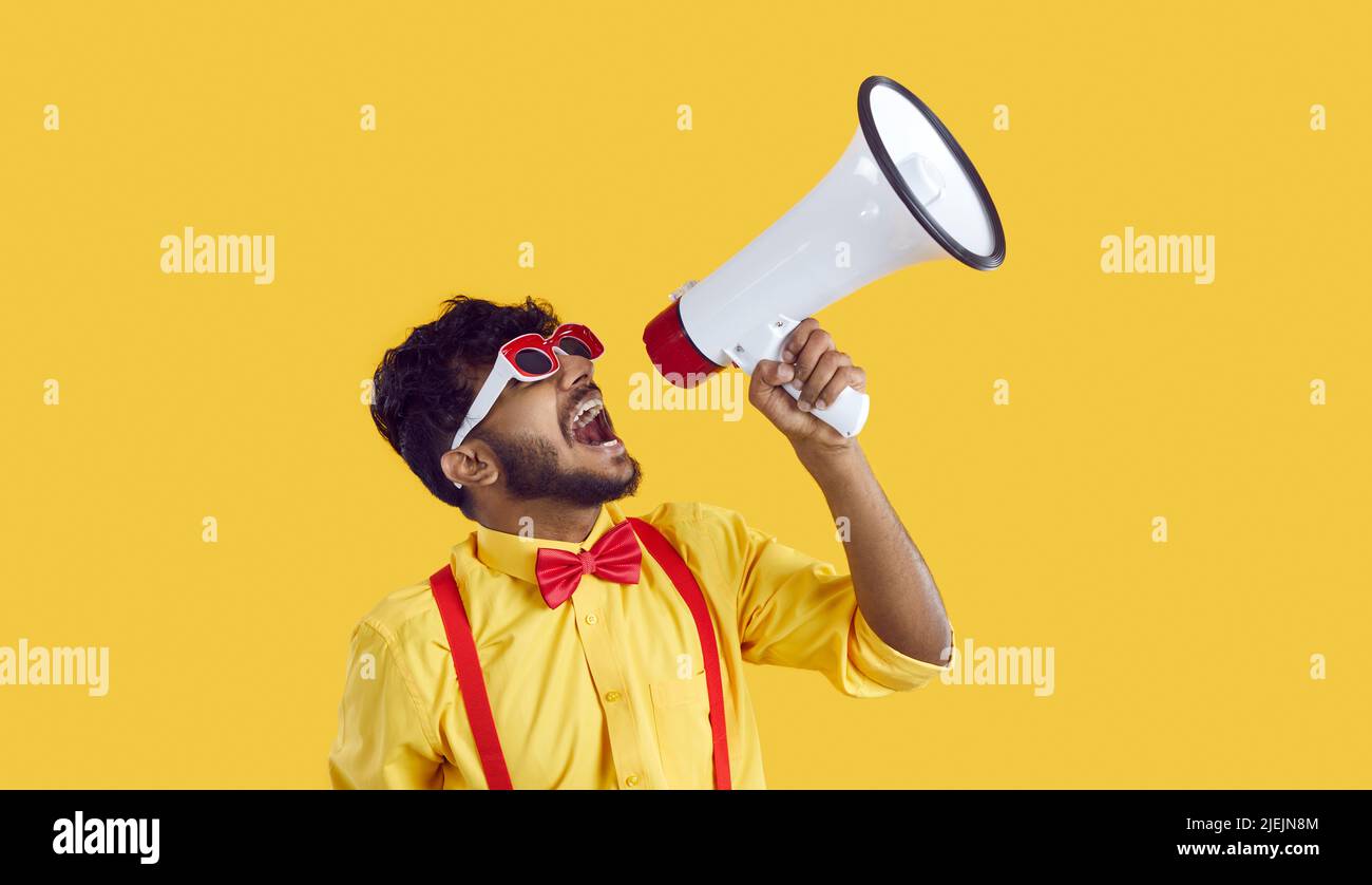 Funny Indian man in humorous clothes makes loud advertisement on vivid yellow background. Stock Photo