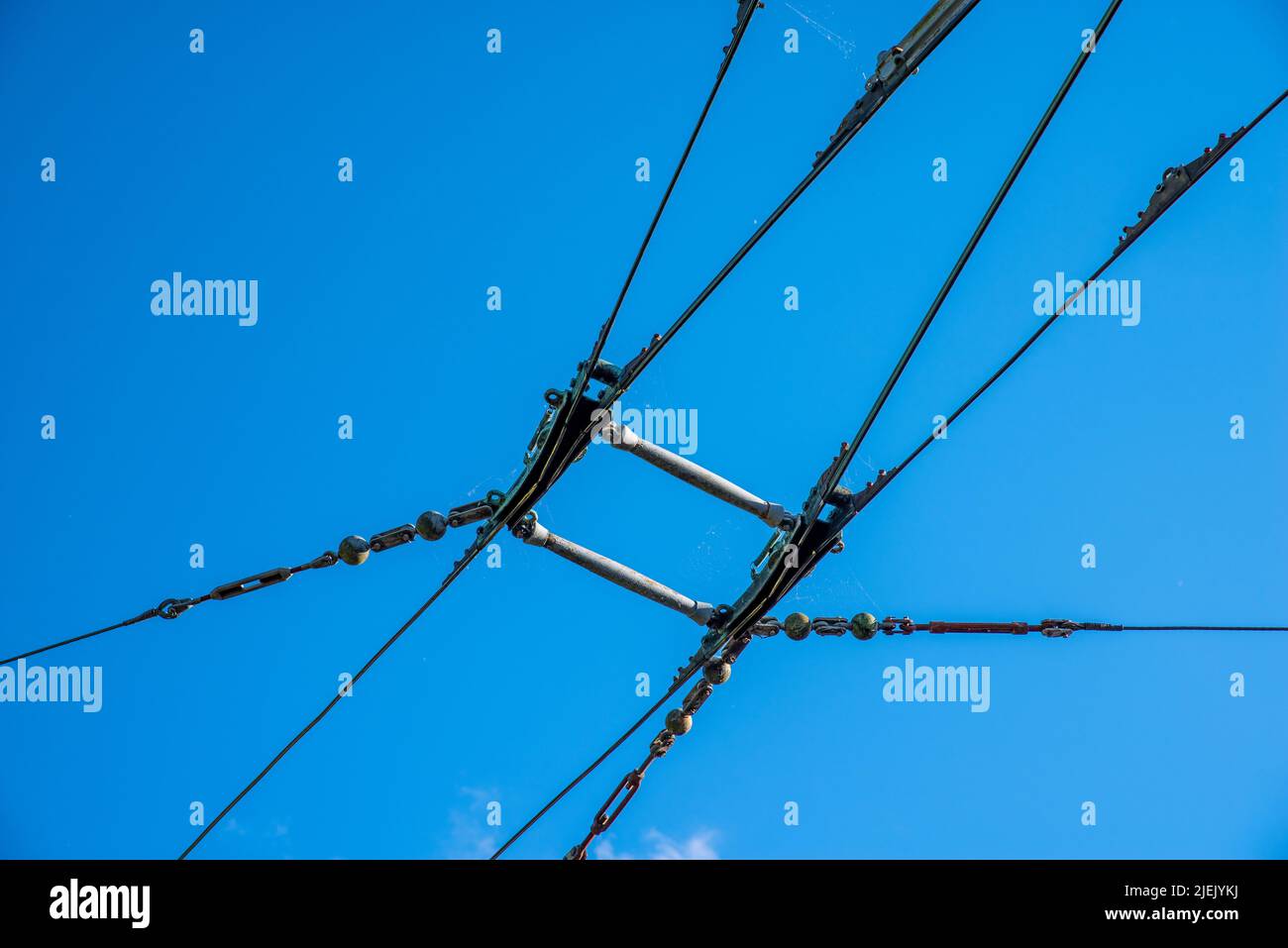 Overhead catenary and contact wires for an electric trolley bus system with a plain blue sky background. Stock Photo