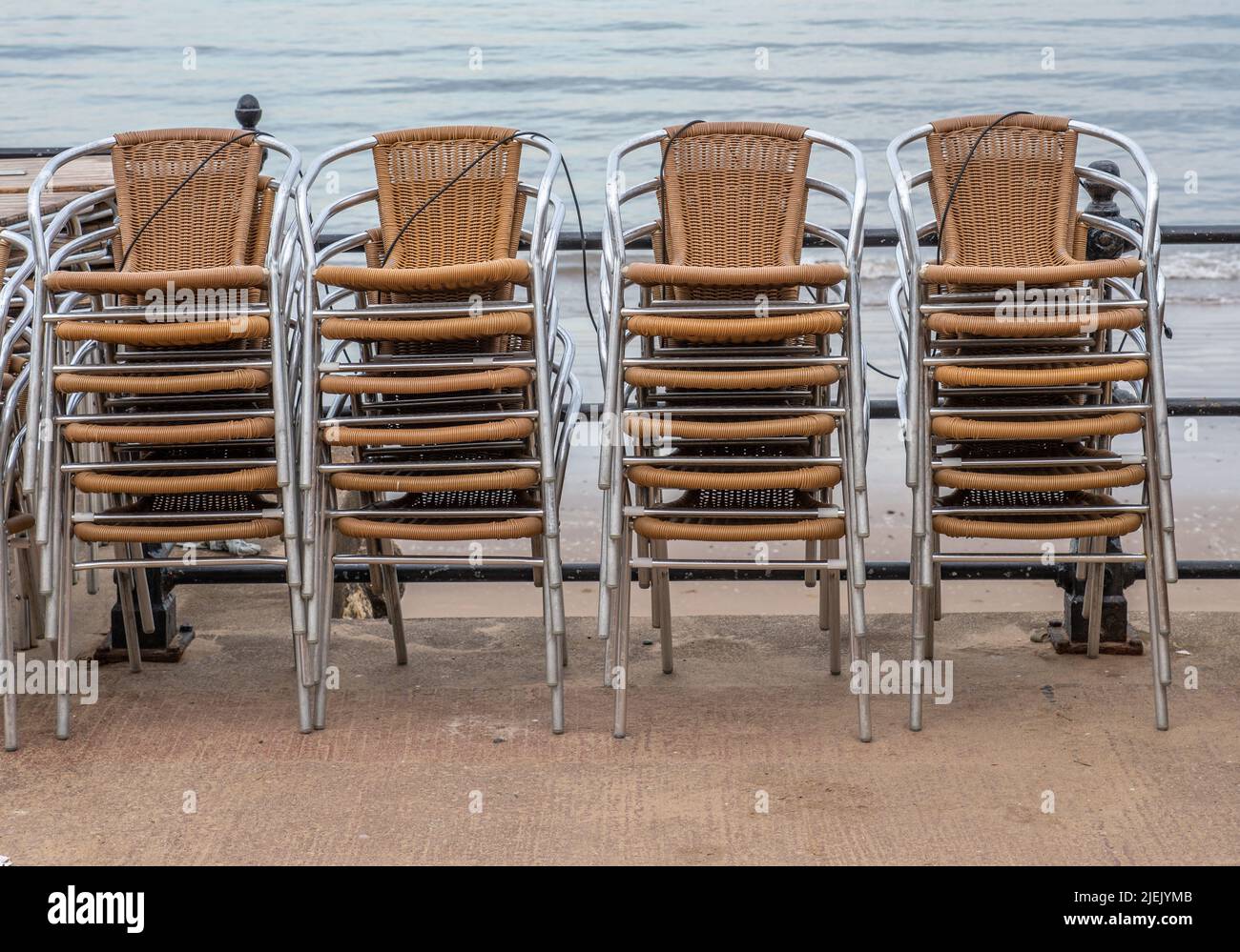 16 June 2022 Scarborough, North Yorkshire, UK - stacks of rattan chairs secured to a metal railing. Stock Photo
