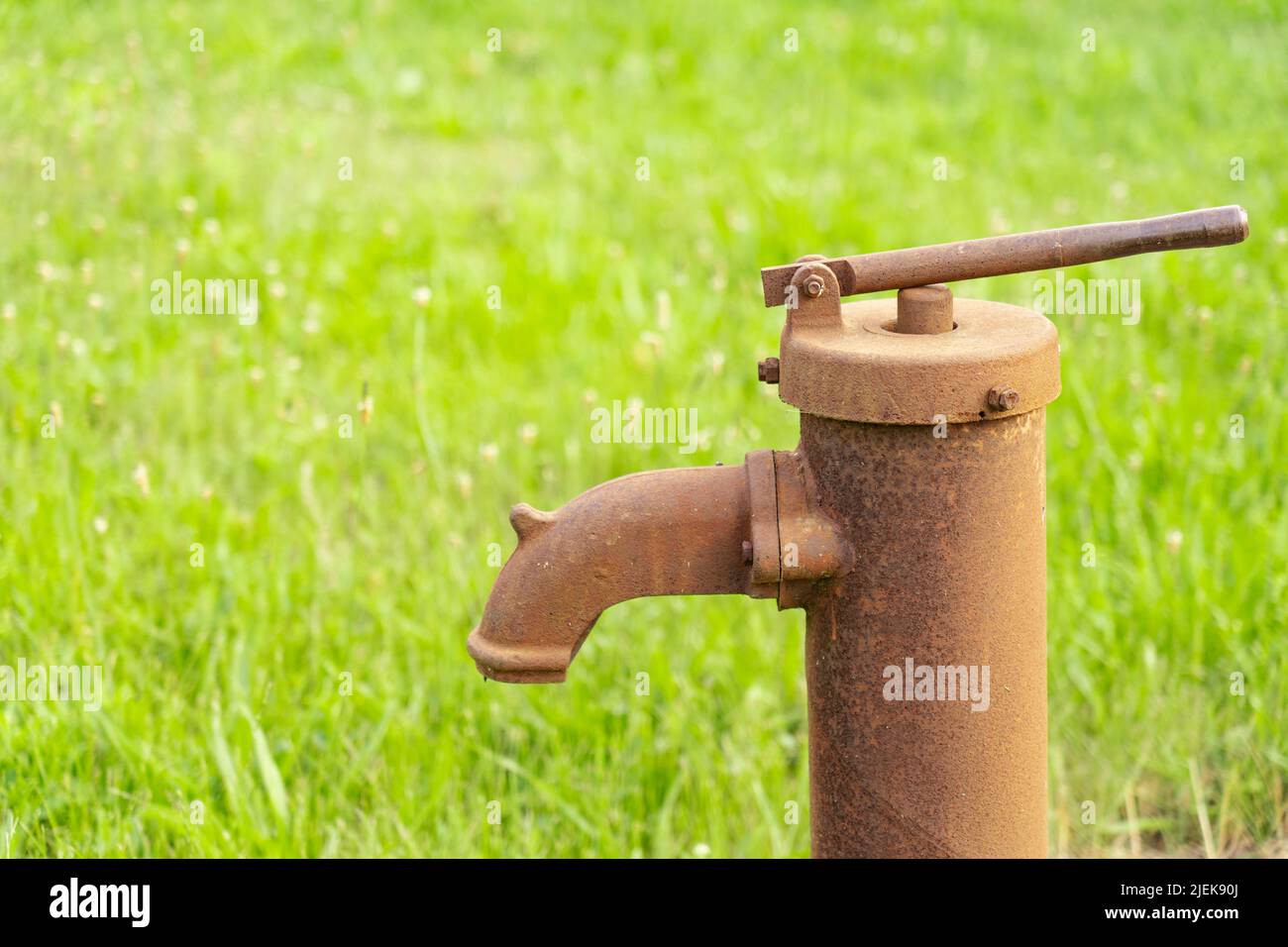 Rusty old hand pump against a blurry background of green grass Stock Photo