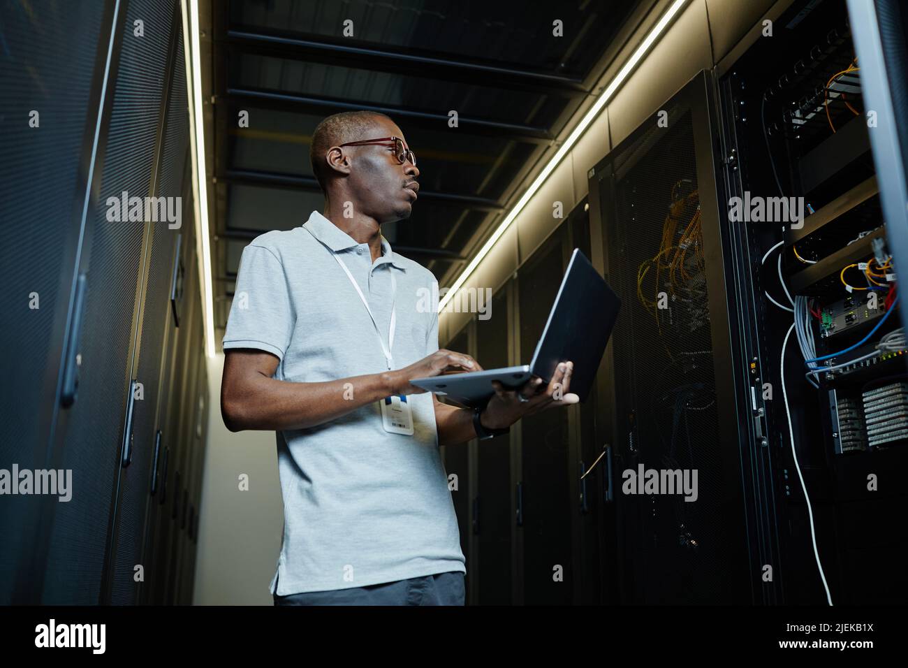 Low angle portrait of African American man managing server network and using laptop, IT technician Stock Photo